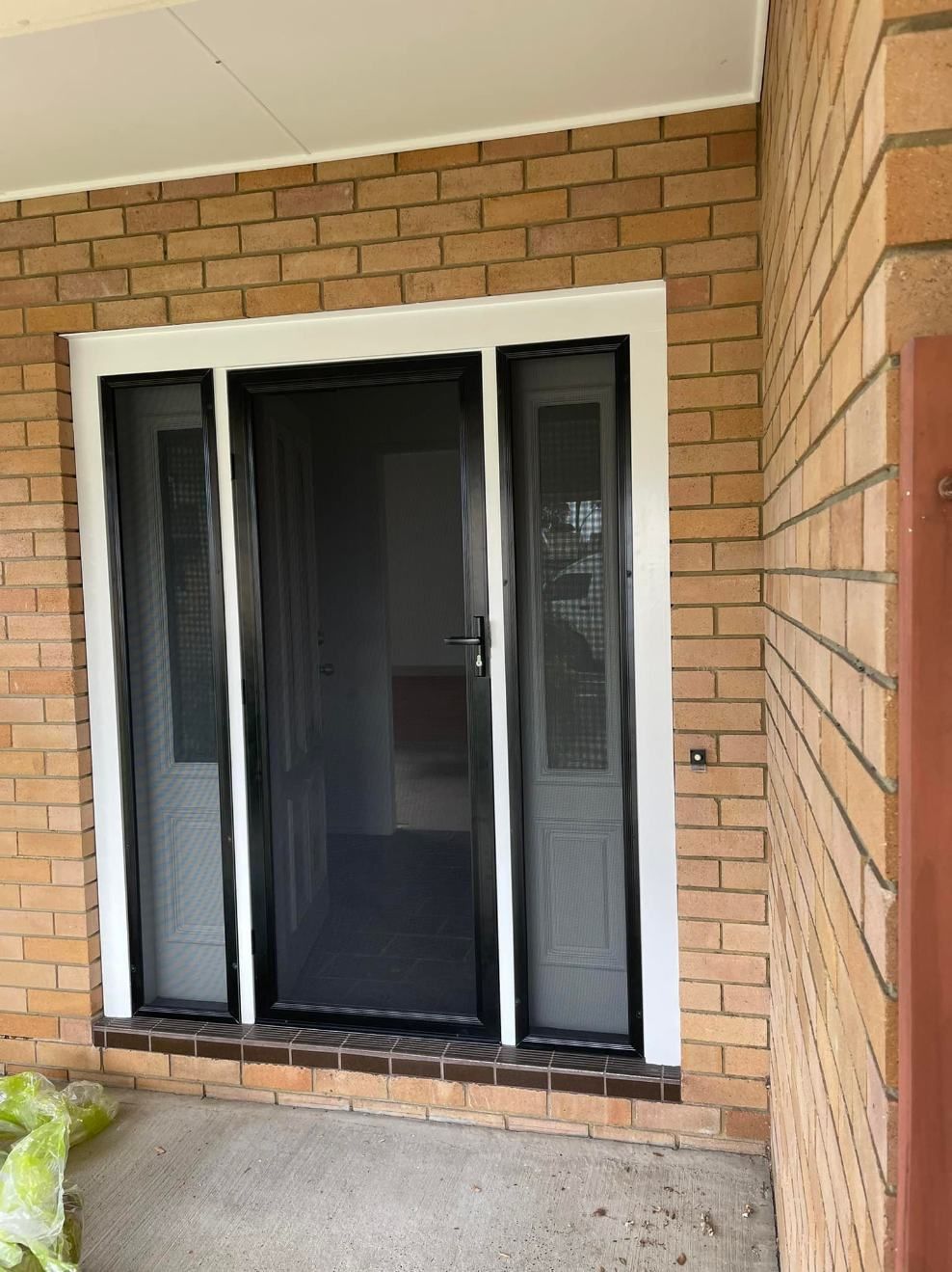 A Brick Building With A Black Screen Door And A White Trim — Central Coast Flyscreen Service In Warnervale, NSW