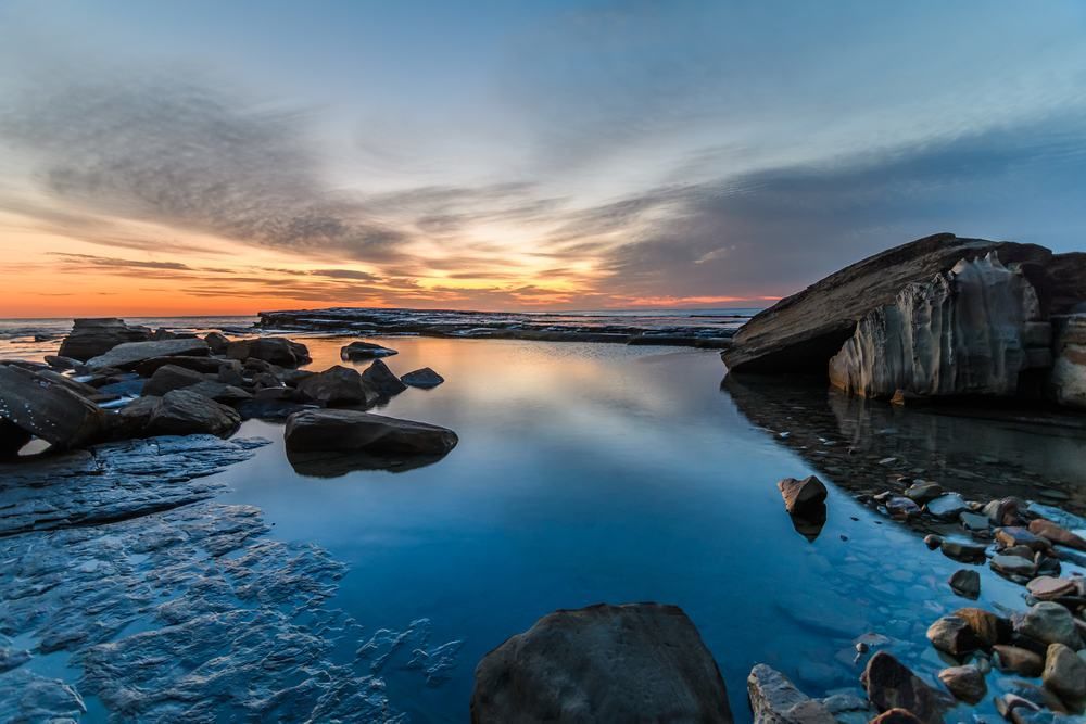 A Sunset Over A Body Of Water With Rocks In The Foreground — Central Coast Flyscreen Service In West Gosford, NSW