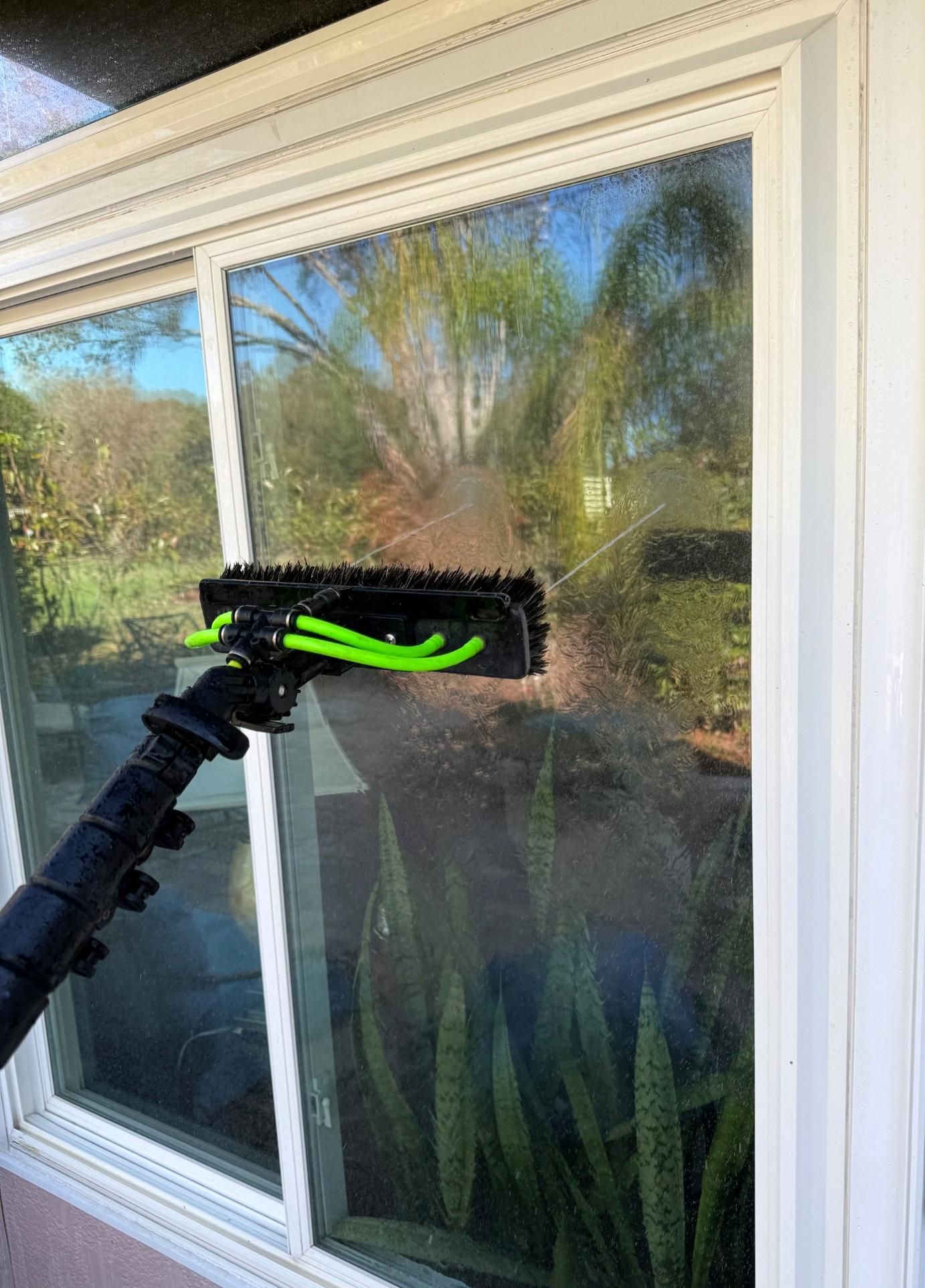 Man in orange coveralls cleaning a large window with a squeegee in a modern kitchen.