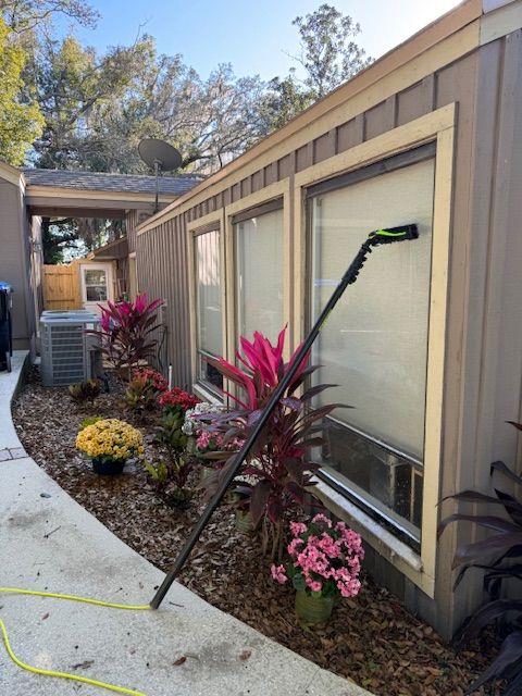 Man in orange coveralls cleaning a large window with a squeegee in a modern kitchen.