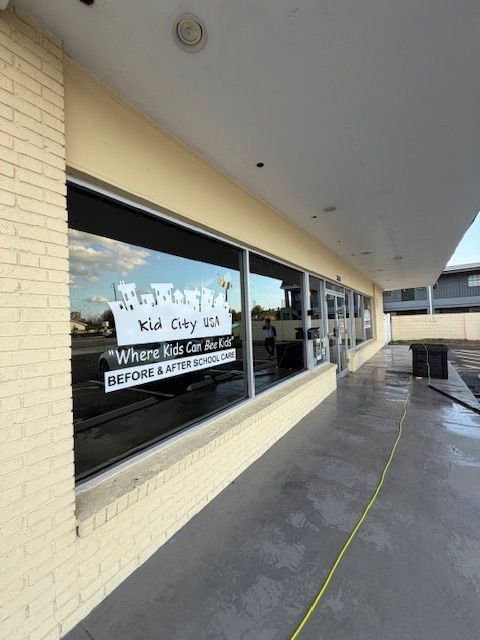 Man wearing black gloves and jacket cleans a window with a squeegee.