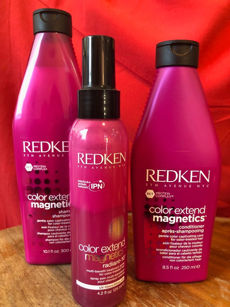 tre bottiglie di prodotti per capelli Redken sono sedute su un tavolo di legno.