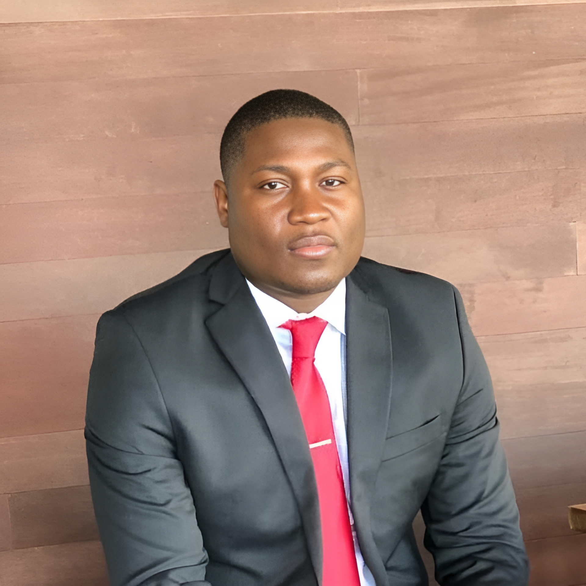 A man in a suit and tie is sitting in front of a wooden wall