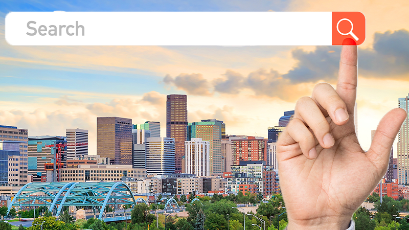 A hand is pointing at a search bar in front of a city skyline.