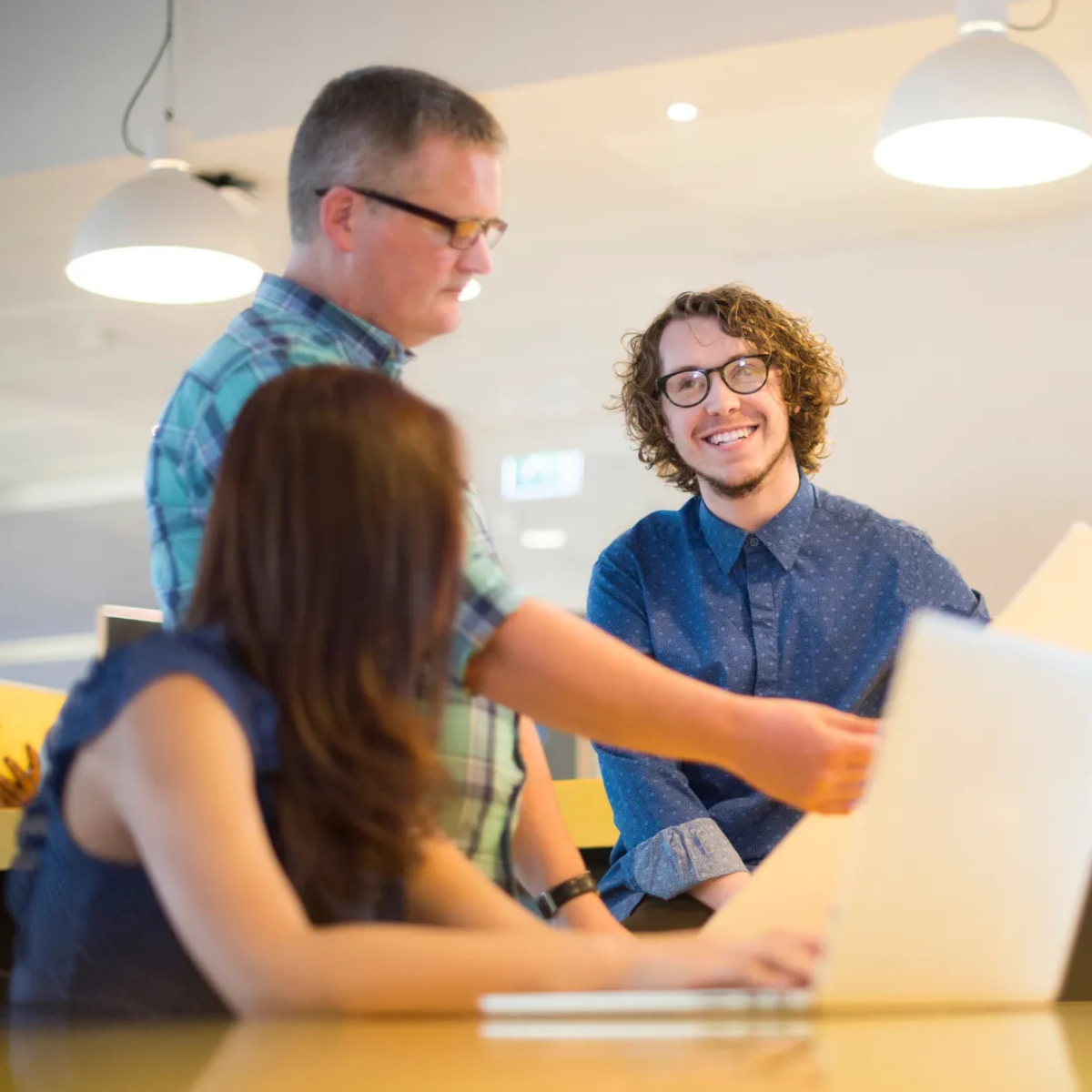 A group of people are sitting around a table looking at a laptop