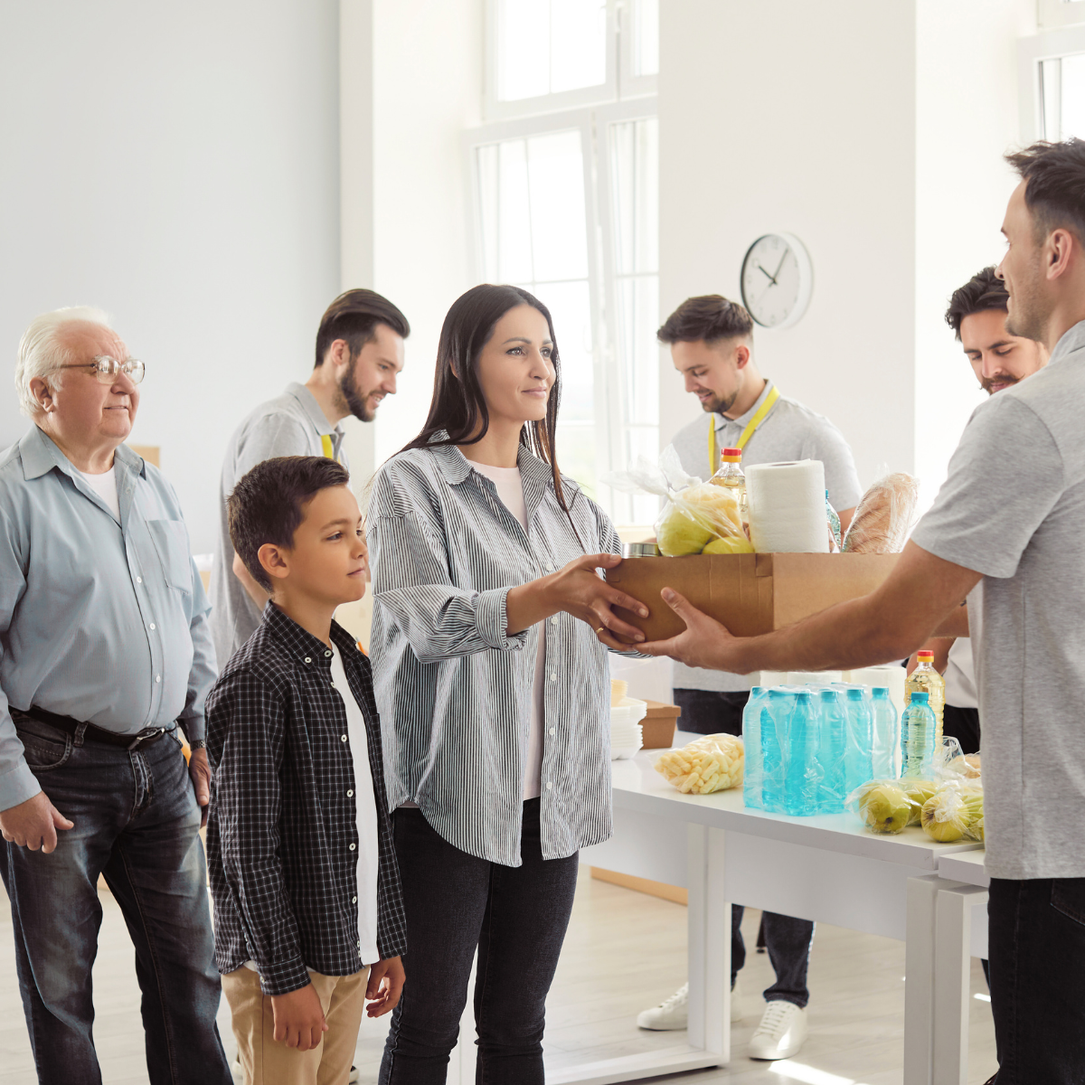 A group of people are standing around a table and a man is giving a box of food to a woman.