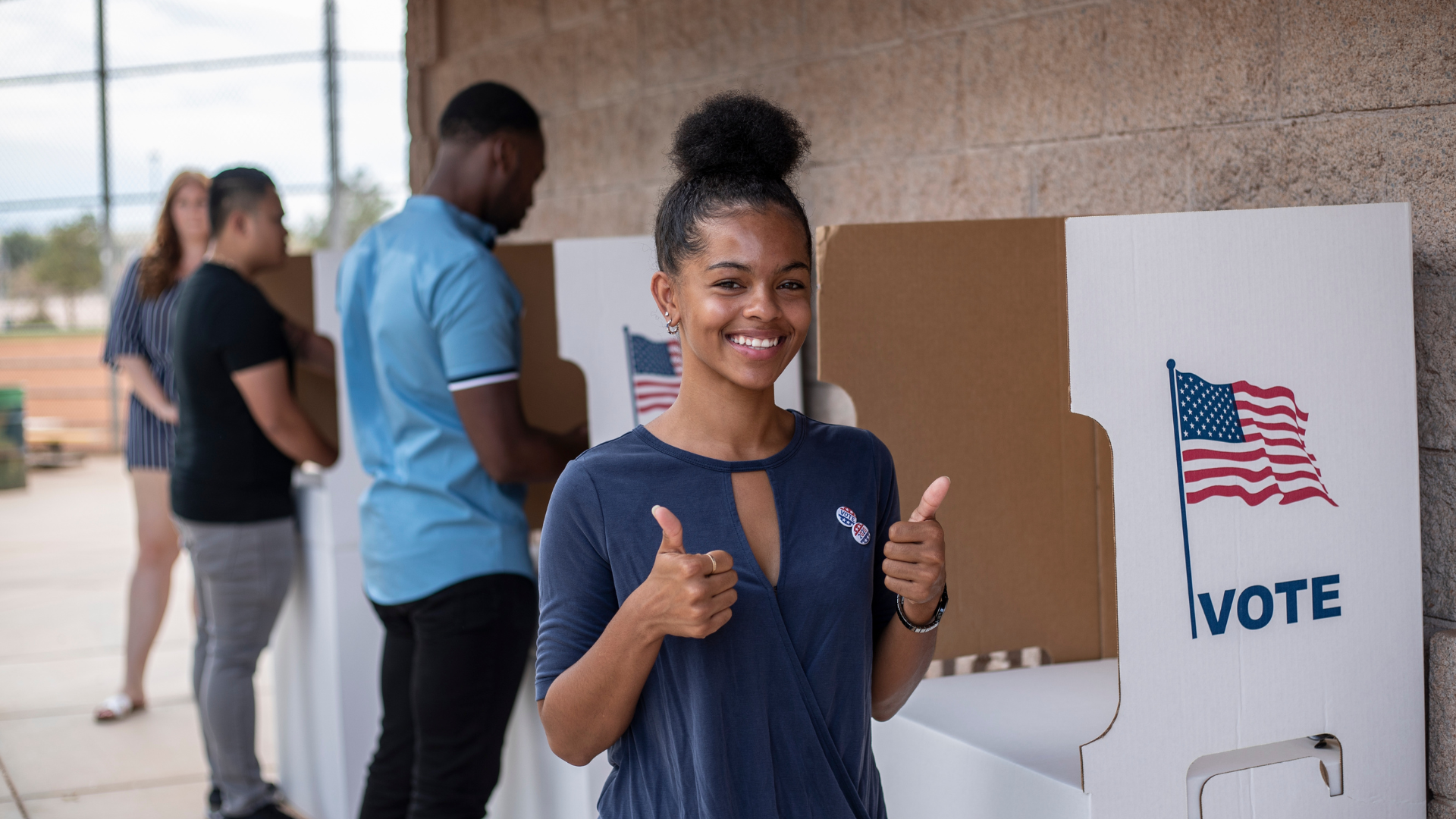 A woman is giving a thumbs up at a voting booth.