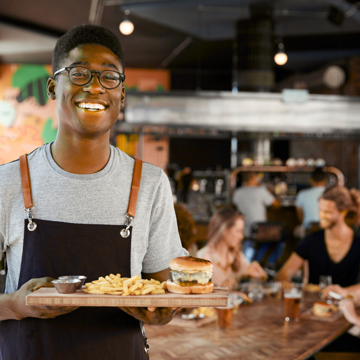 A man in an apron is holding a tray of food in a restaurant.