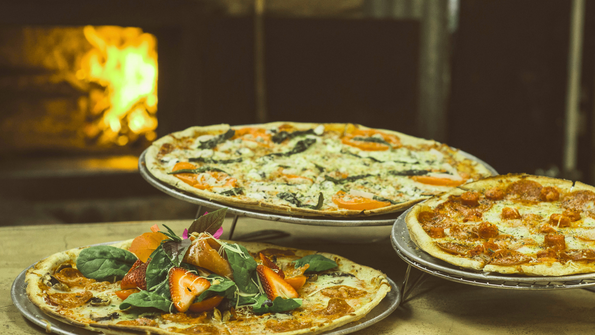 Three pizzas are stacked on top of each other on a table in front of an oven.