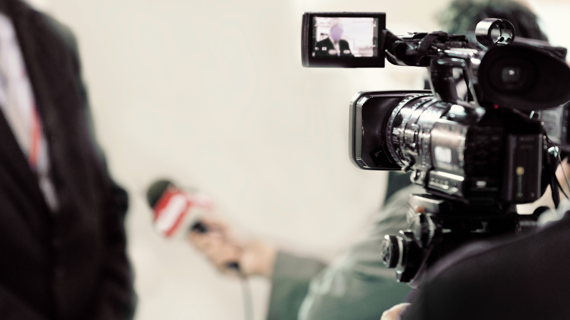 A man in a suit is being interviewed by a cameraman while holding a microphone.