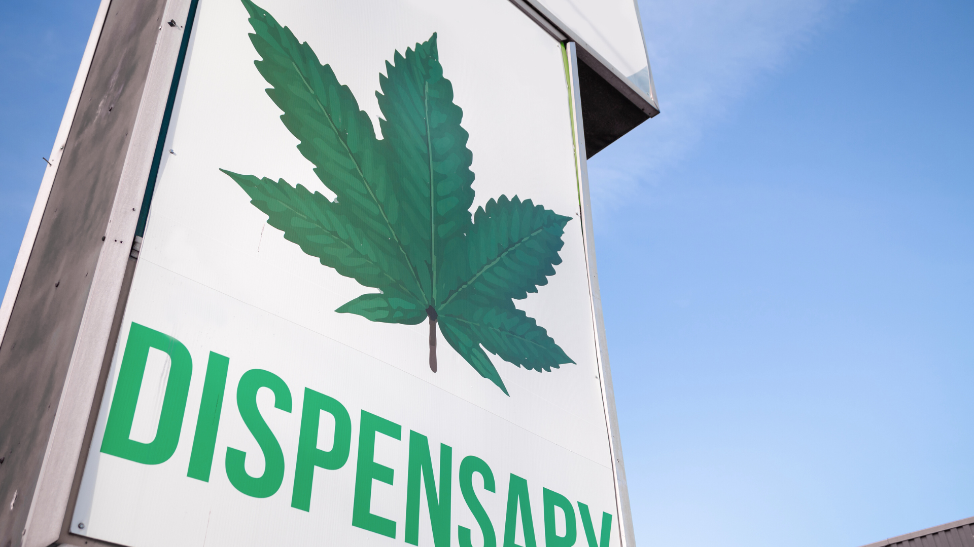 Dispensary sign with a green cannabis leaf on a white background against a blue sky