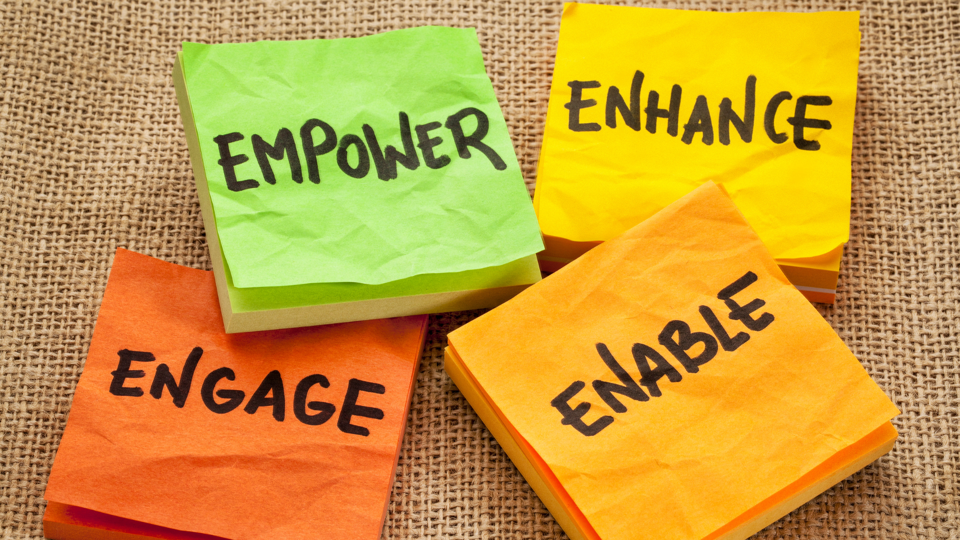 Four sticky notes with the words empower enhance engage and enable written on them