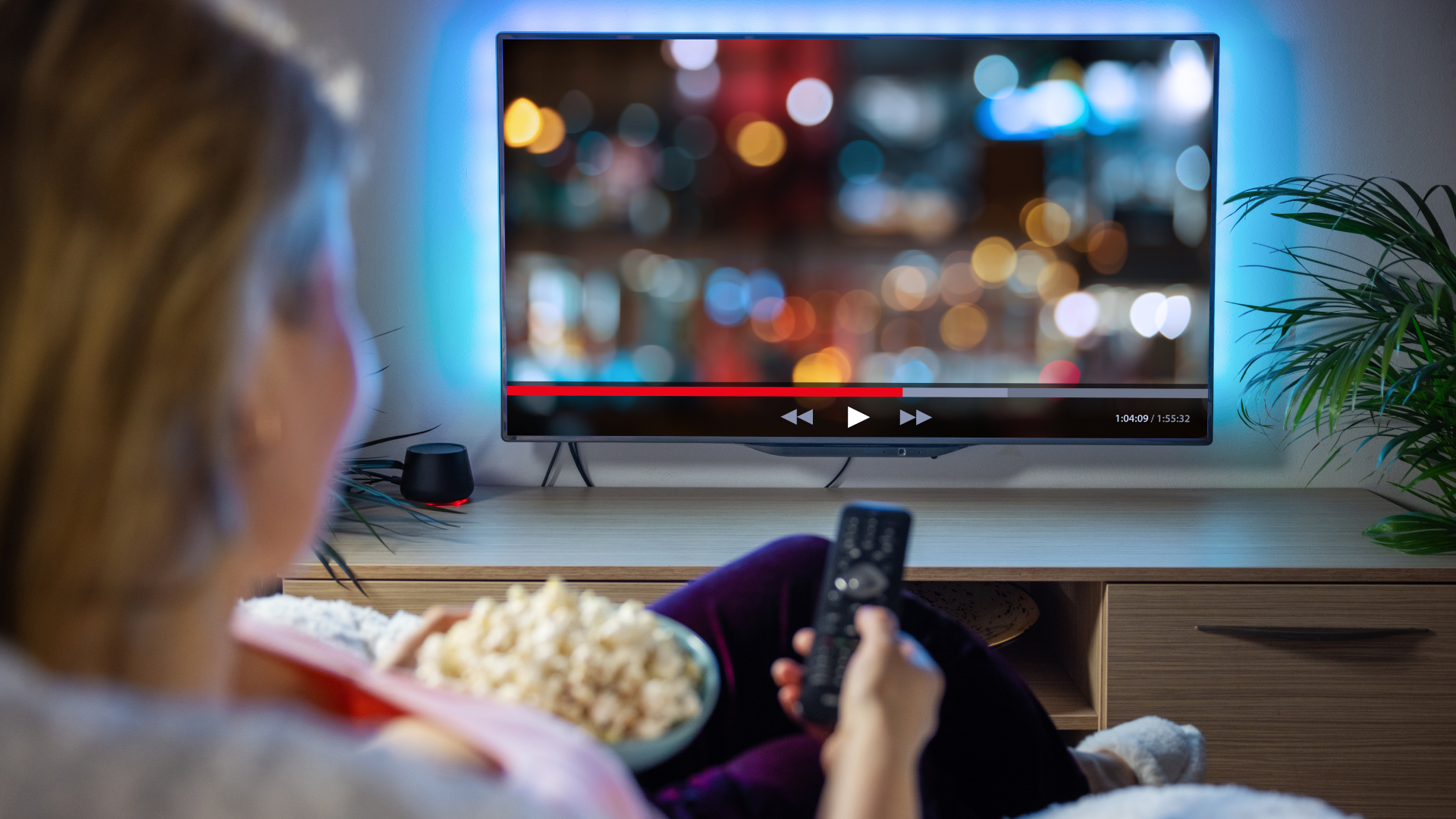 A woman is sitting on a couch holding a remote control while watching tv.