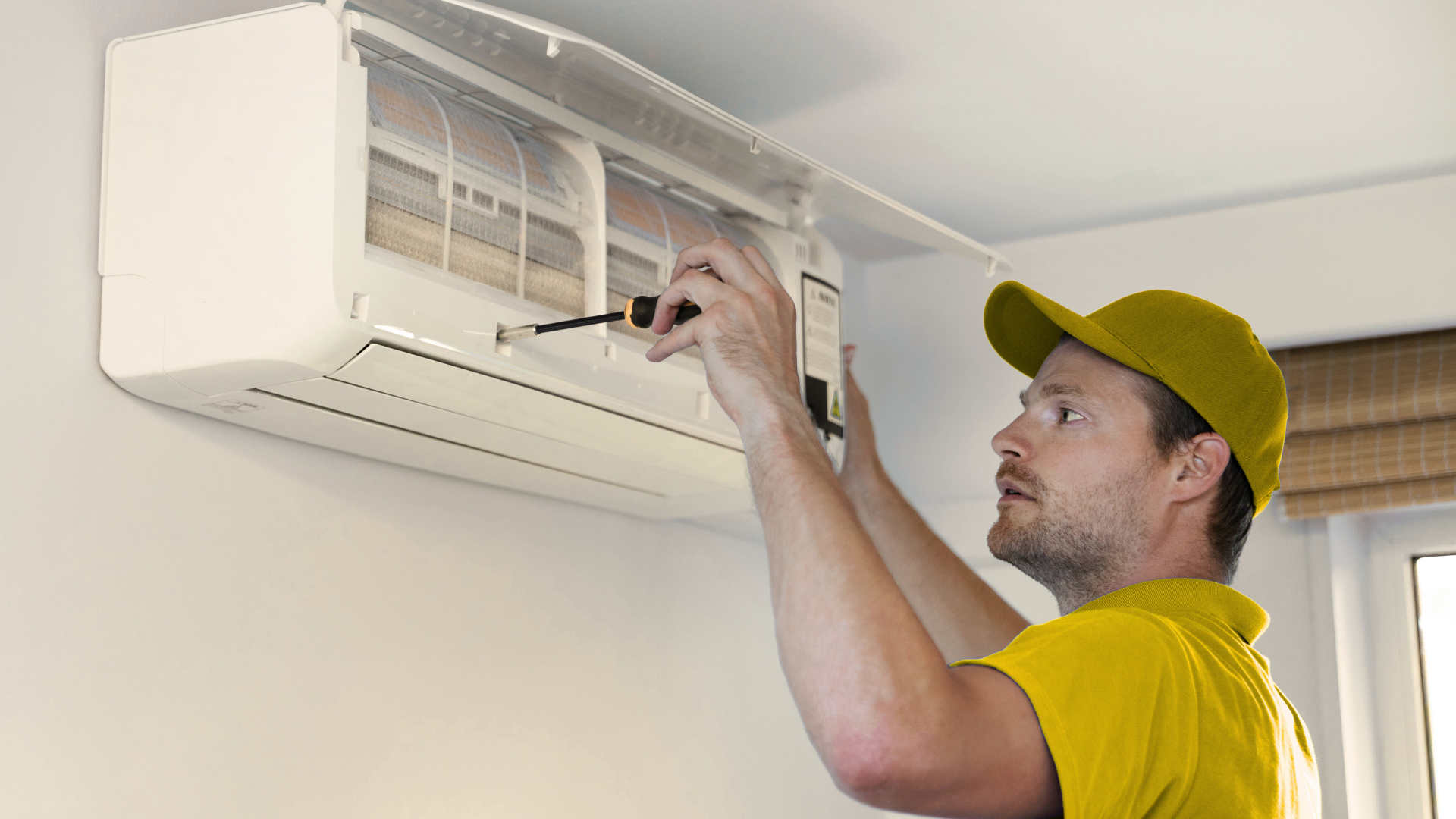 A man is fixing an air conditioner with a screwdriver.