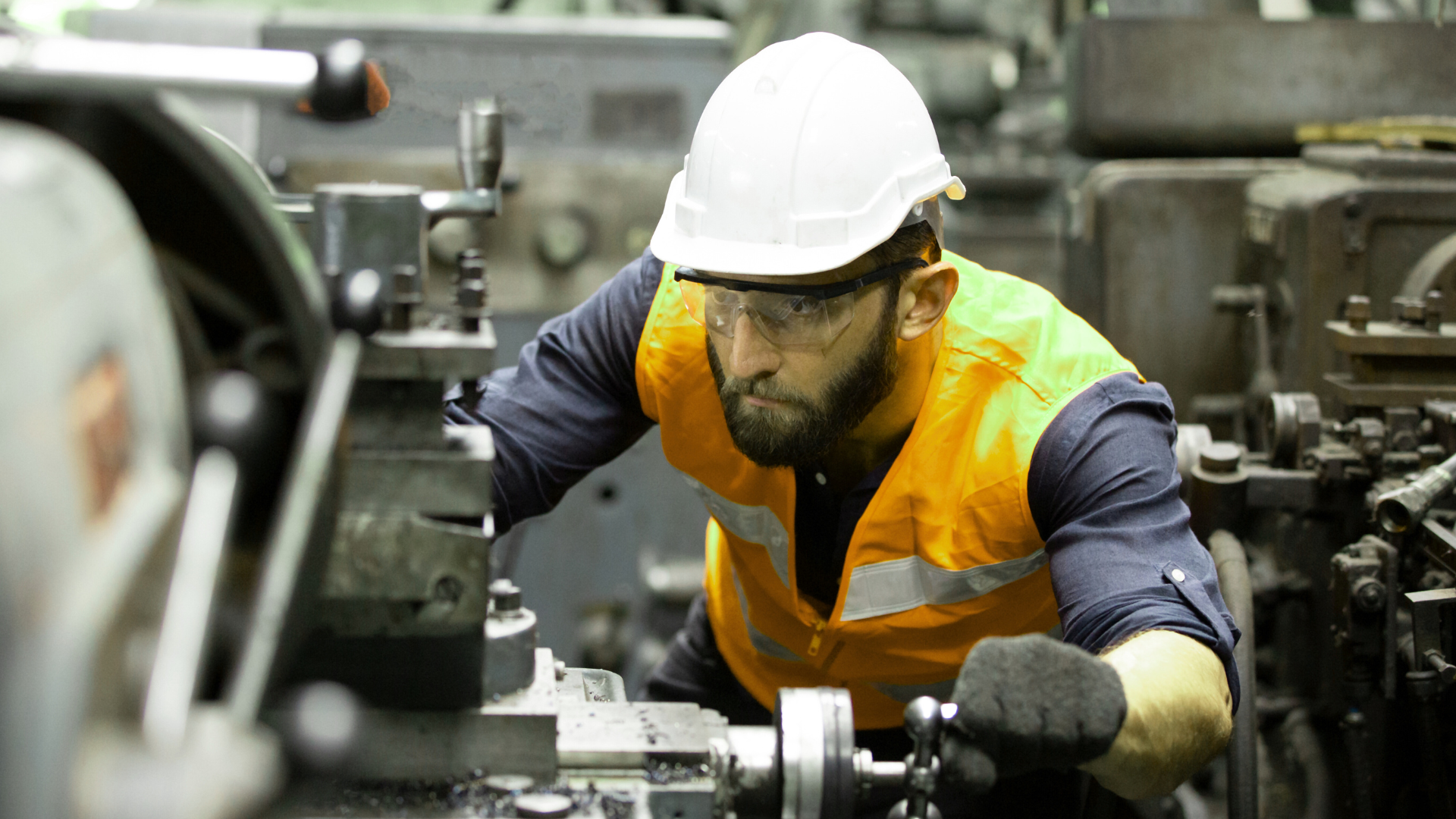 A man wearing a hard hat and safety vest is working on a machine in a factory.