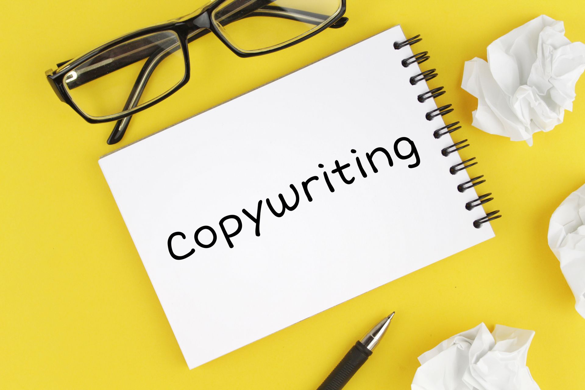 A notebook with the word copywriting written on it next to a pen and glasses.