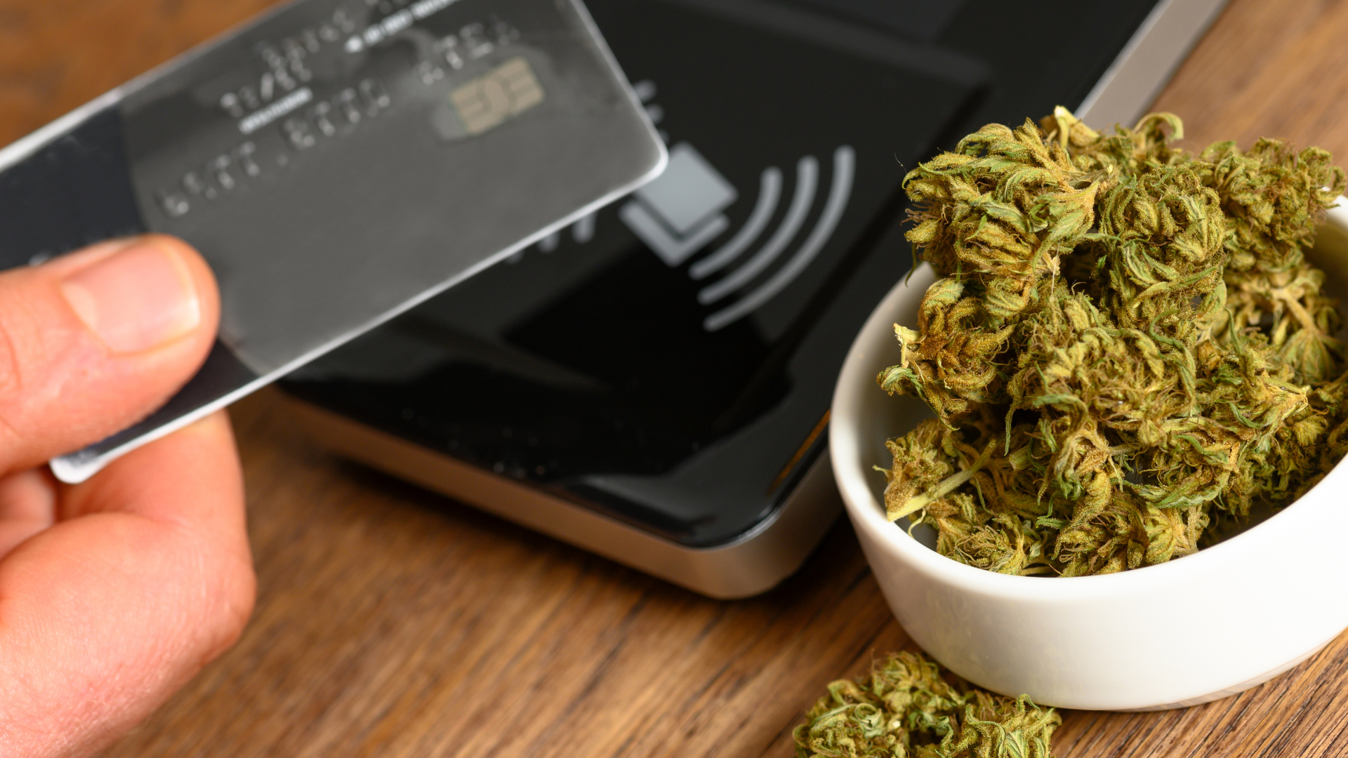 Person using a scoop to handle cannabis near a digital payment terminal