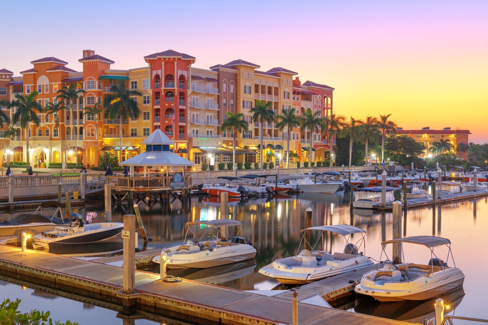 A marina with boats docked in front of a building at sunset.