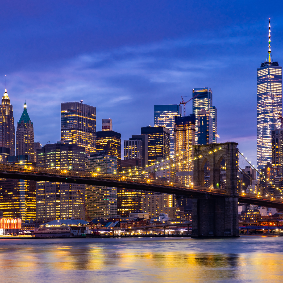 A bridge over a body of water in front of a city skyline at night.