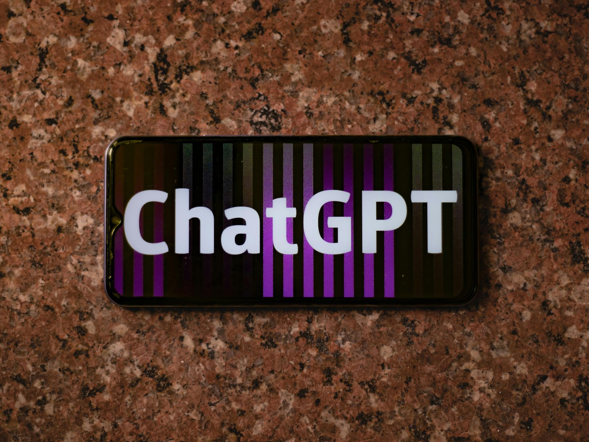 Smartphone displaying the ChatGPT logo on a brown granite surface.