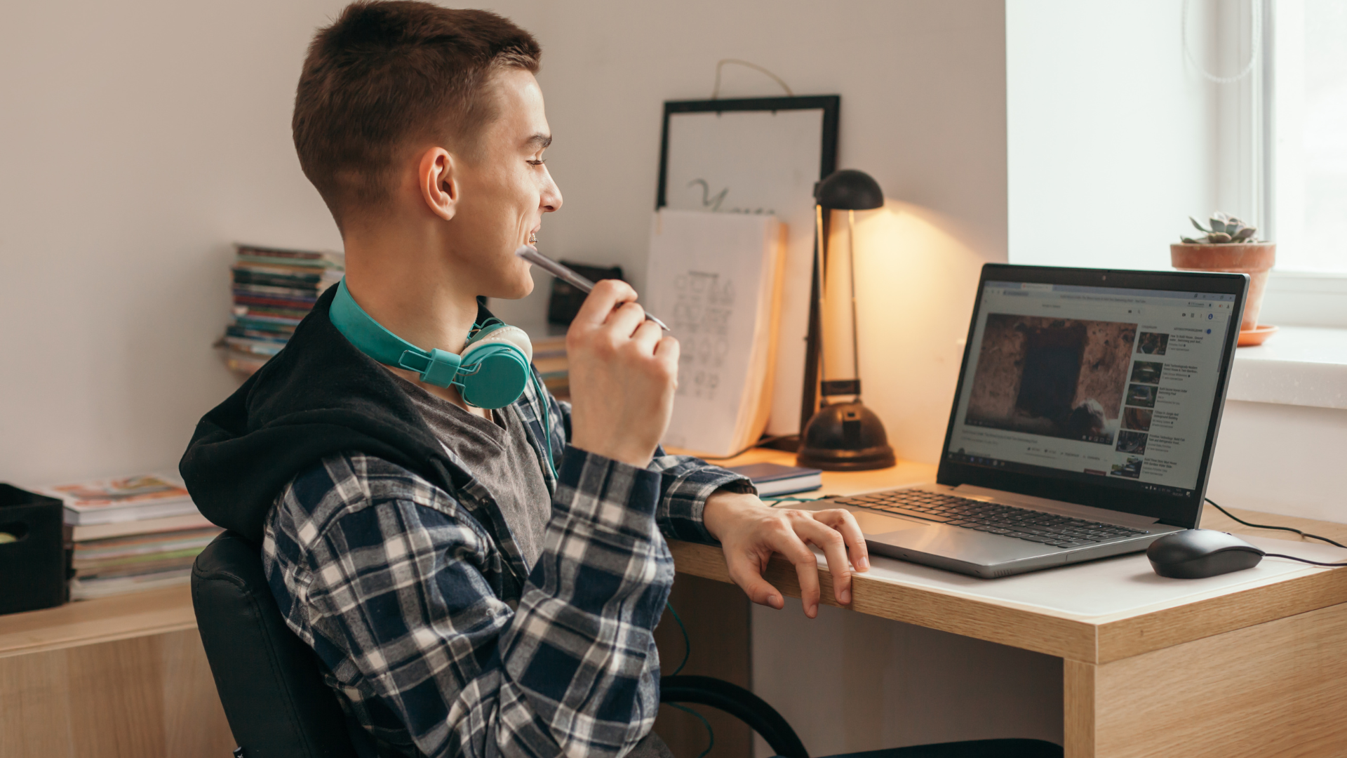 A young man is sitting at a desk using a laptop computer.