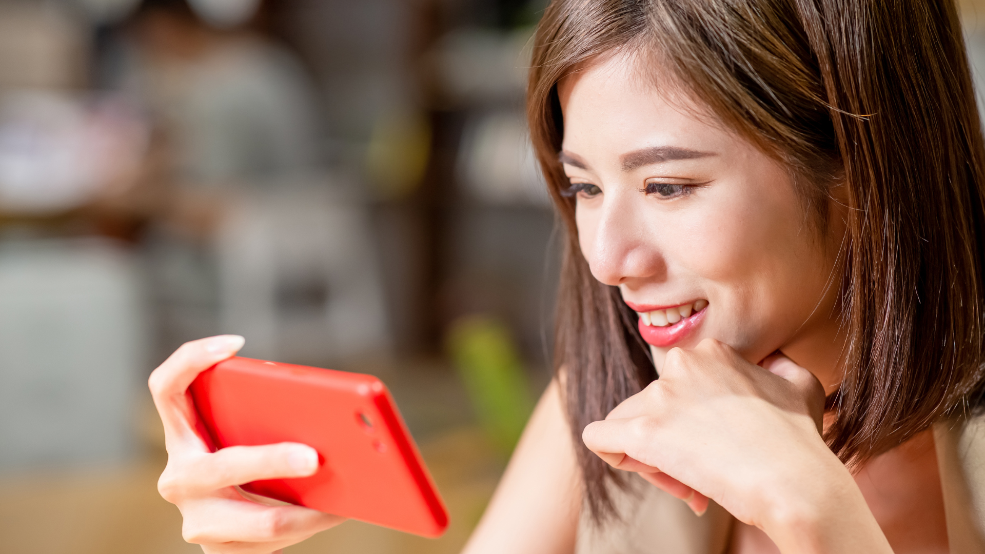 A woman is holding a red cell phone in her hand and smiling.