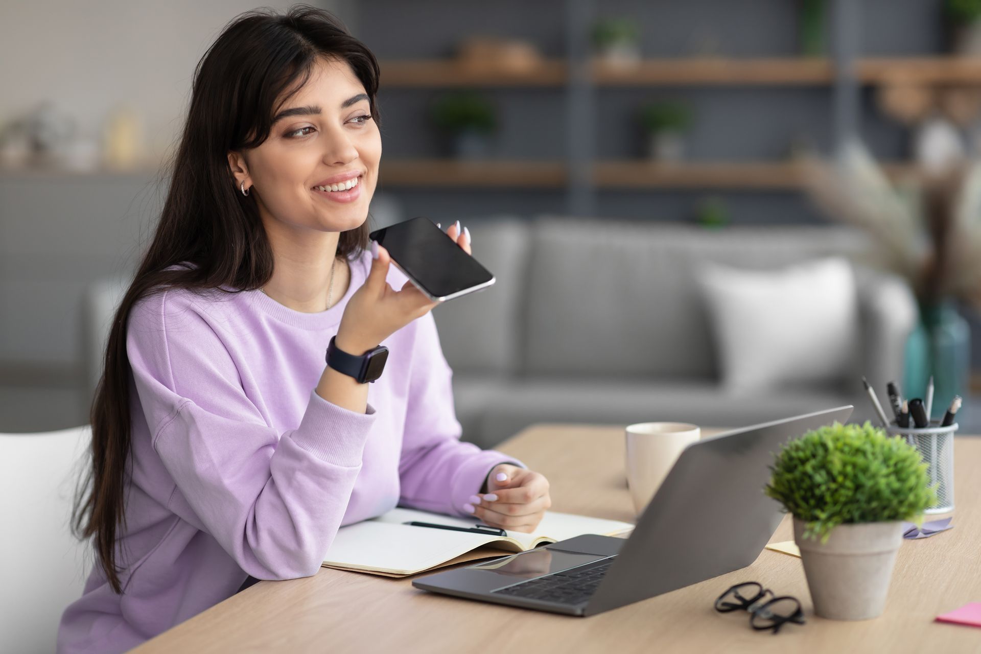 A woman is sitting at a desk with a laptop and a cell phone.