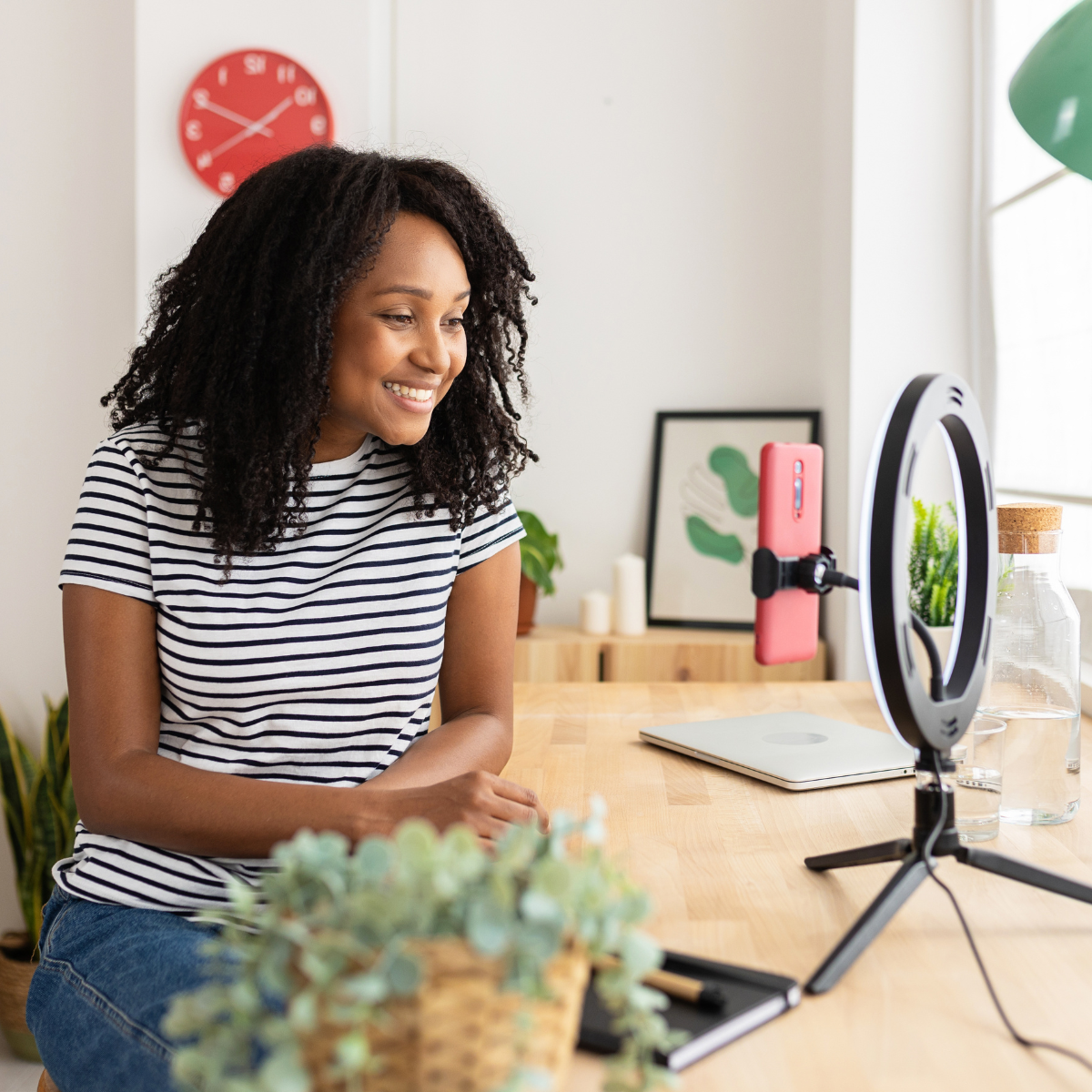 A woman is sitting at a desk using a laptop and a cell phone.