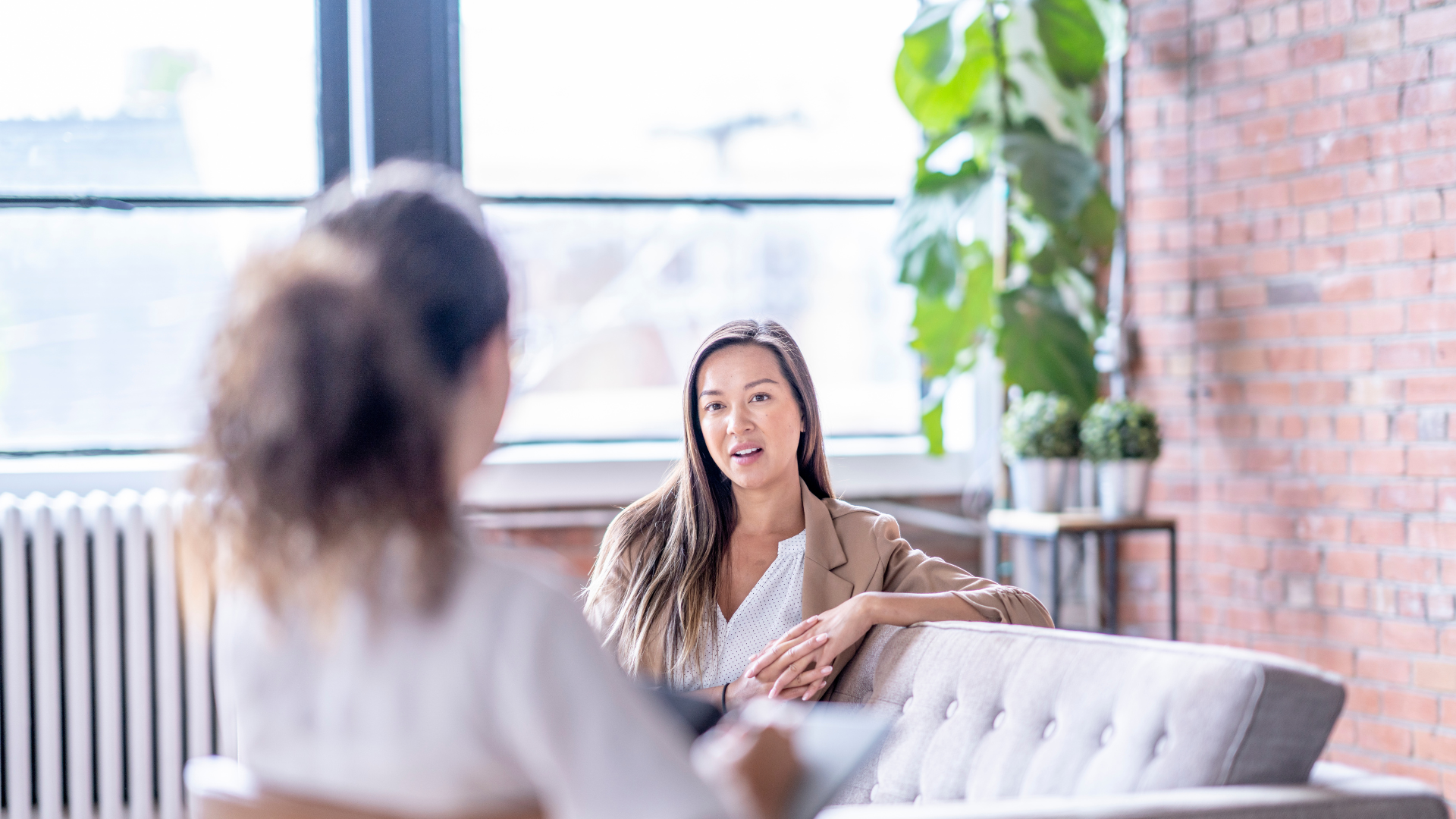 Two women are sitting on a couch having a conversation.