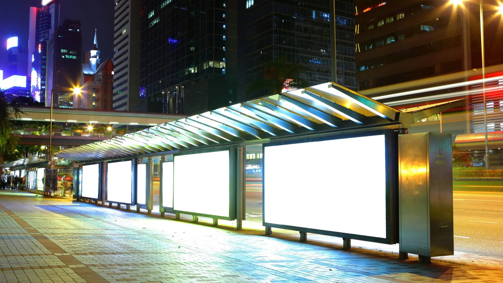 A bus stop with a lot of billboard signs at night