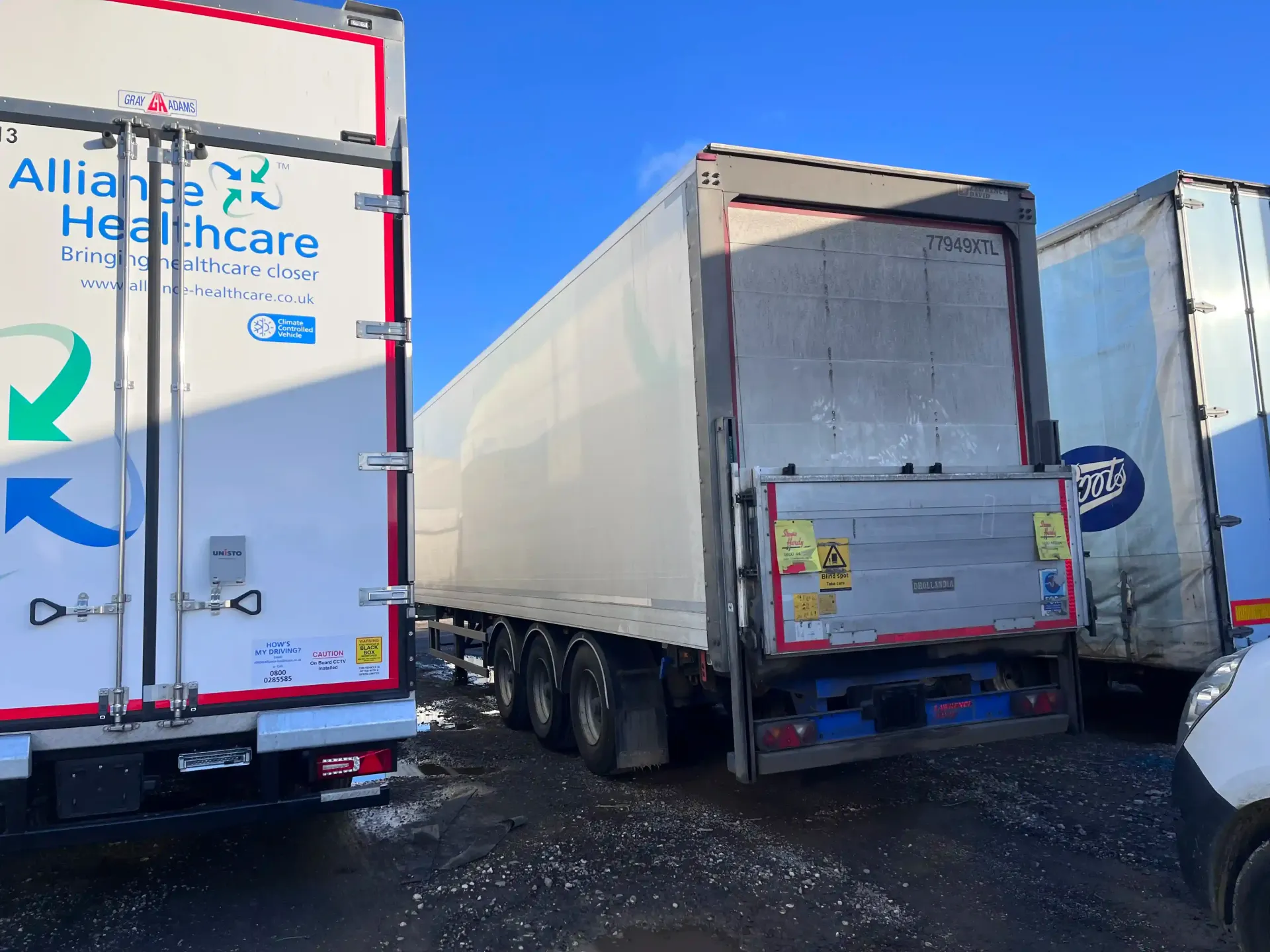 Three large parked freight trailers in a lot under a clear blue sky, one clearly marked 