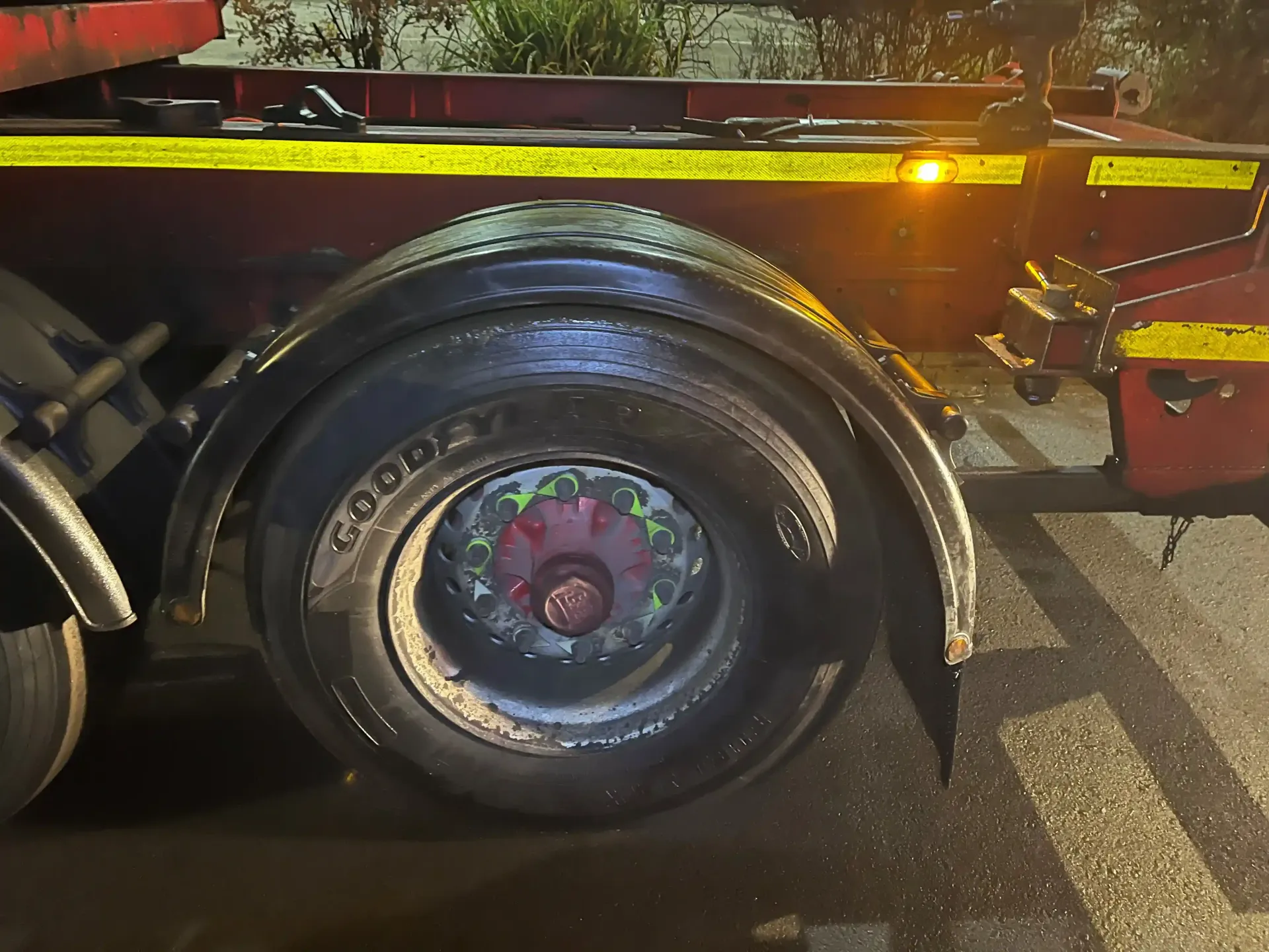 A close-up view of a large black truck tire and wheel fender, showing the red hub and yellow reflective tape on the frame.