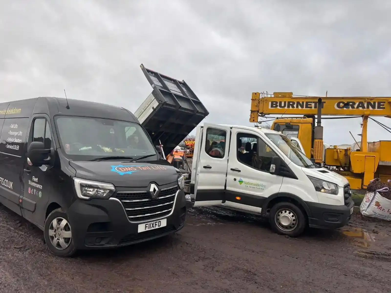 A black Renault van and a white Ford van parked on a muddy site, with a yellow Burnett crane in the background.