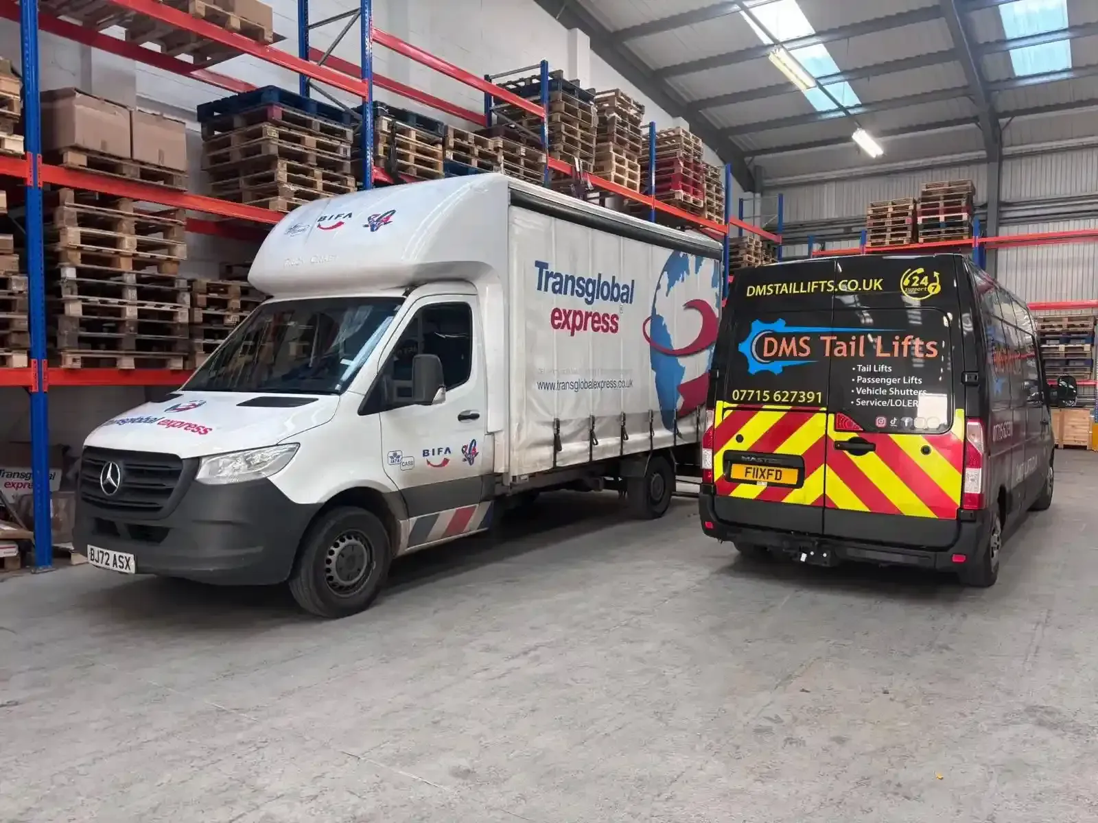 Two delivery vehicles, a white box truck and a black van with yellow safety stripes, parked inside a warehouse.