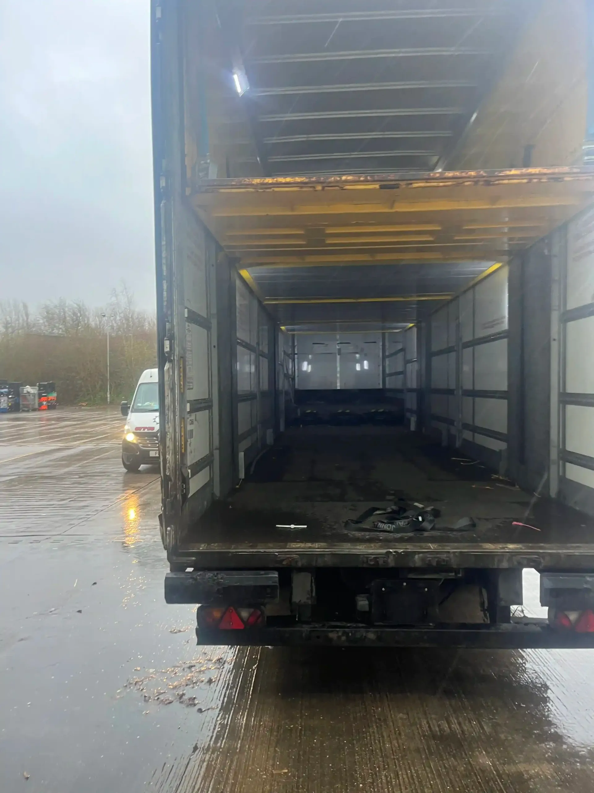 Open rear view of a semi-trailer truck parked in a wet, muddy outdoor lot on an overcast day.