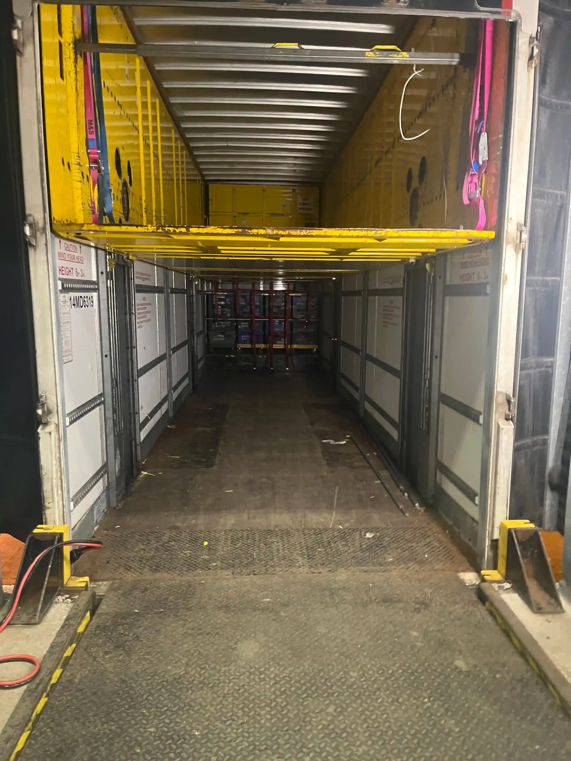 View through a loading dock doorway into an empty semi-trailer with yellow retractable shelving units.