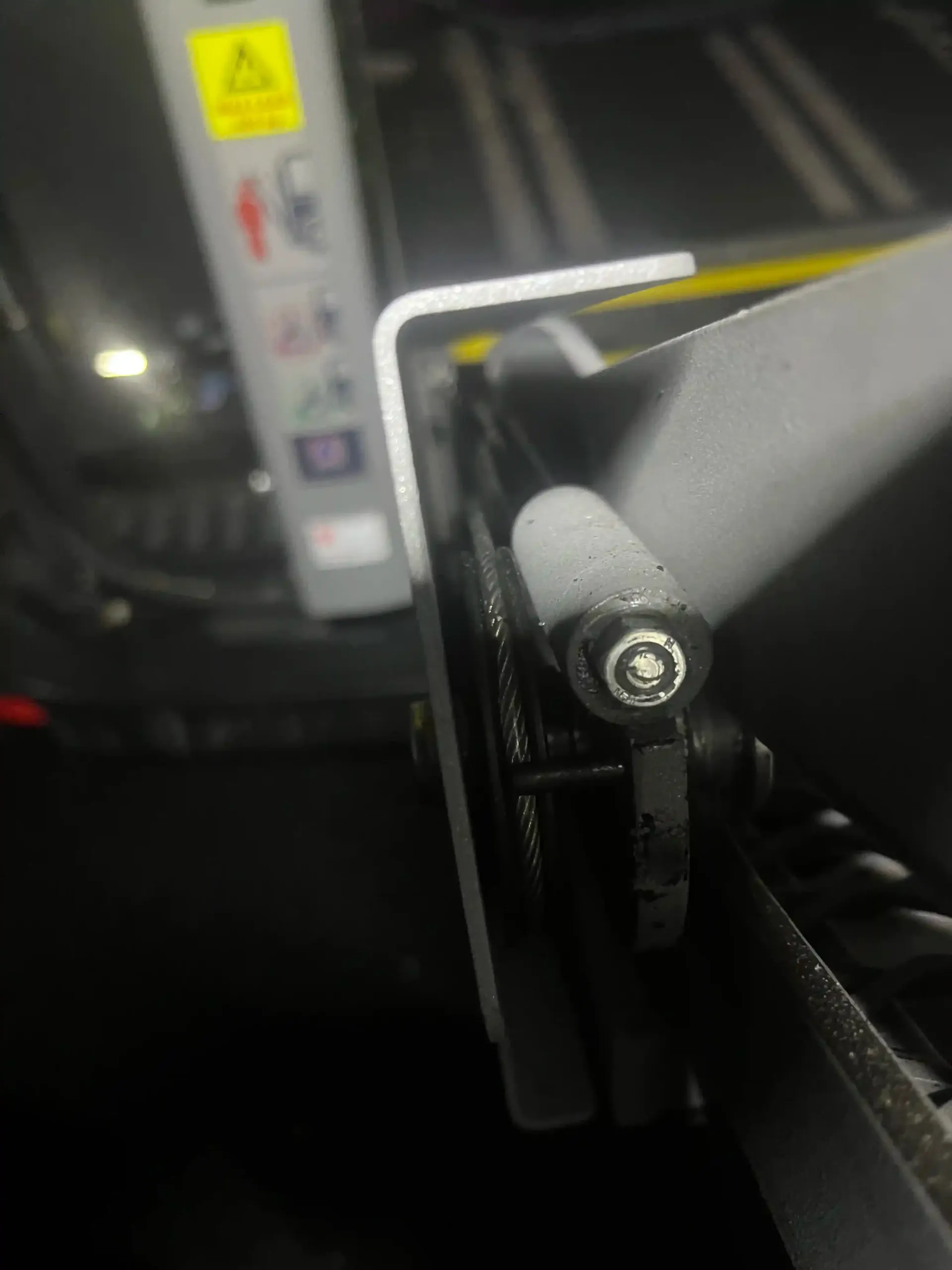 Close-up of a metal bracket assembly with a black bolt and a safety warning label visible in the background.