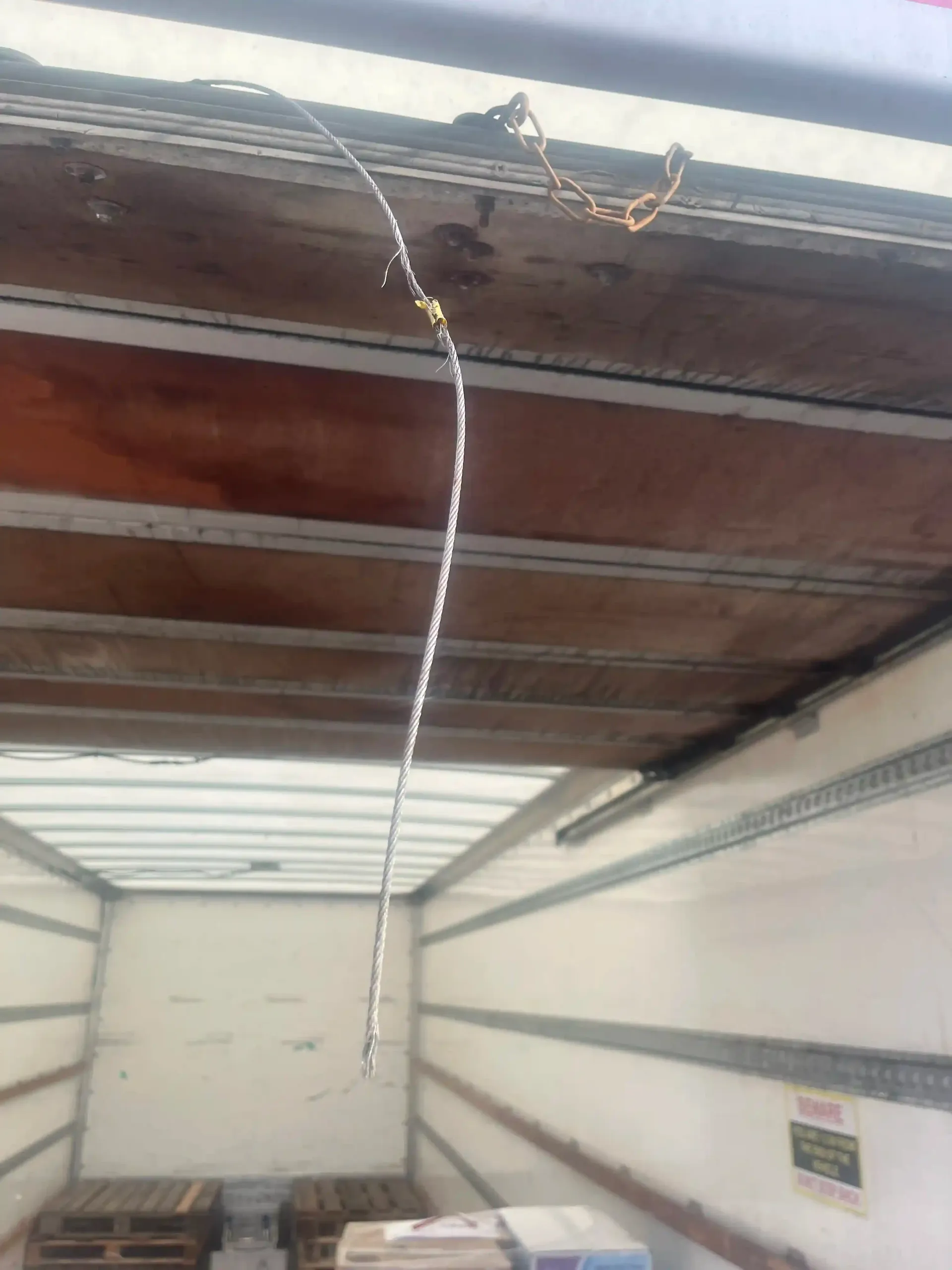 A thin, white, dangling pull cord hangs from the ceiling inside the empty cargo area of a truck.