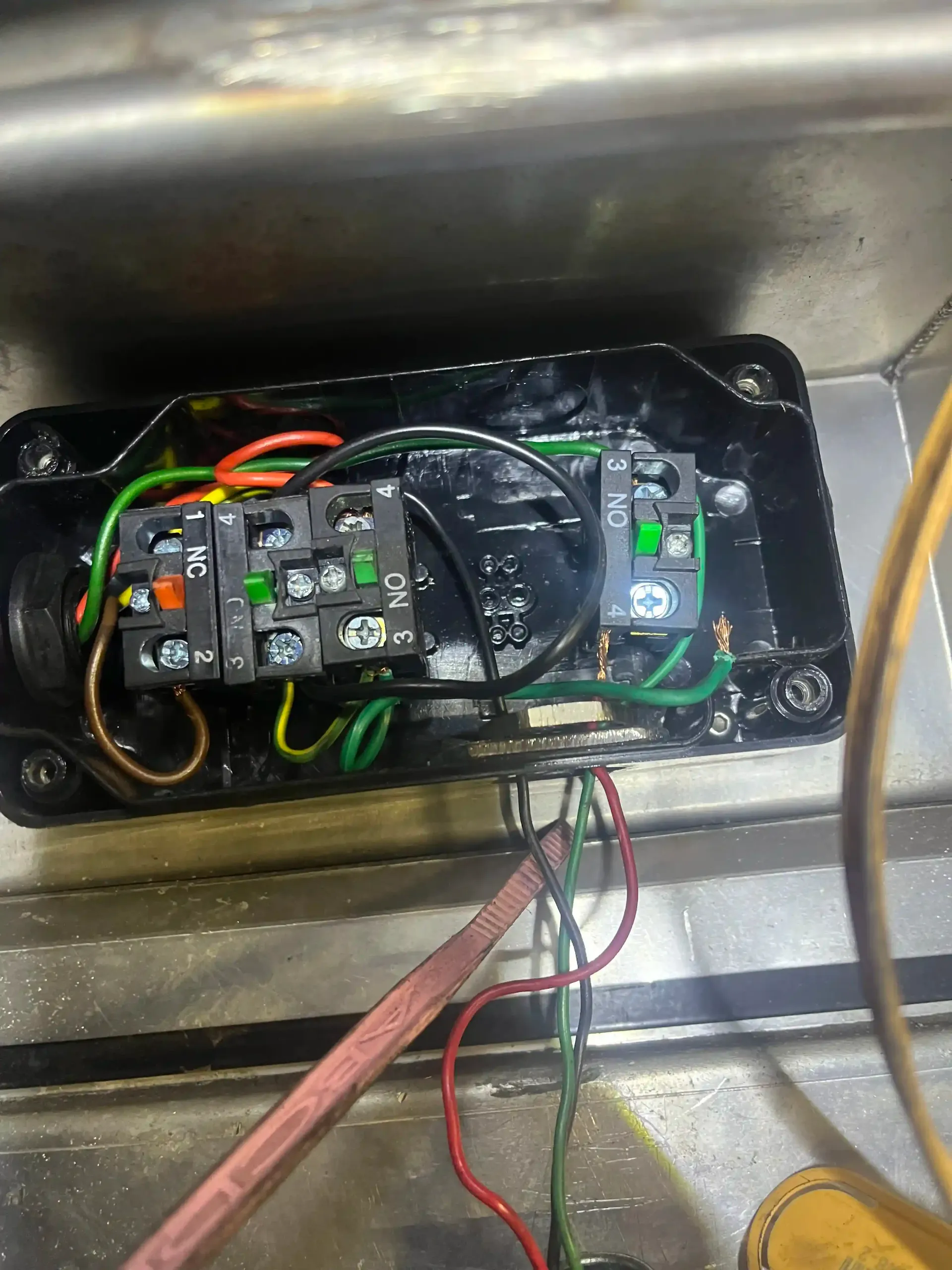 An open electrical junction box with green, black, and red wiring connected to terminal blocks inside a metal enclosure.