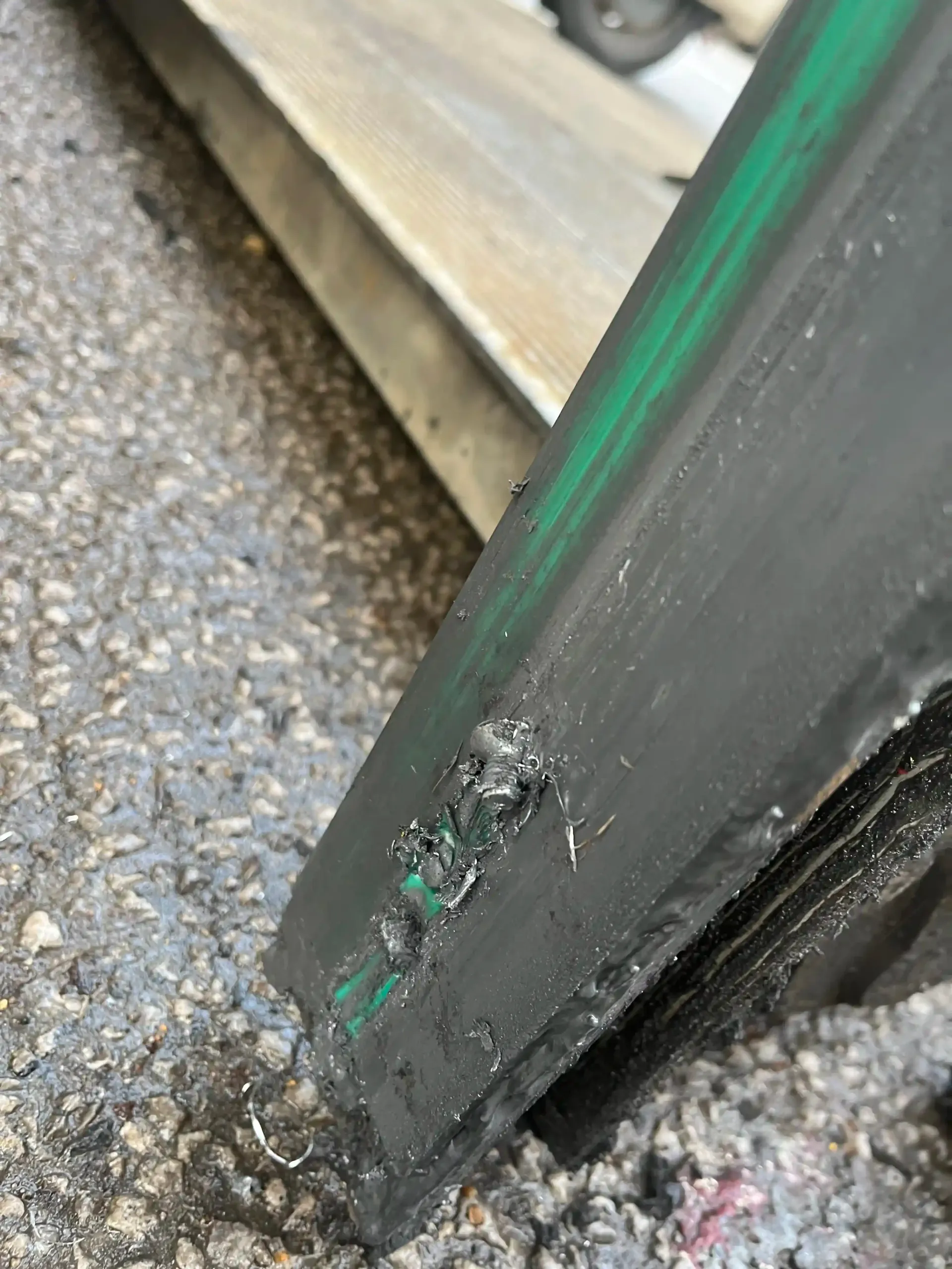 Close-up of a dark rubber tire tread showing a deep puncture or tear revealing a green inner cord or liner.