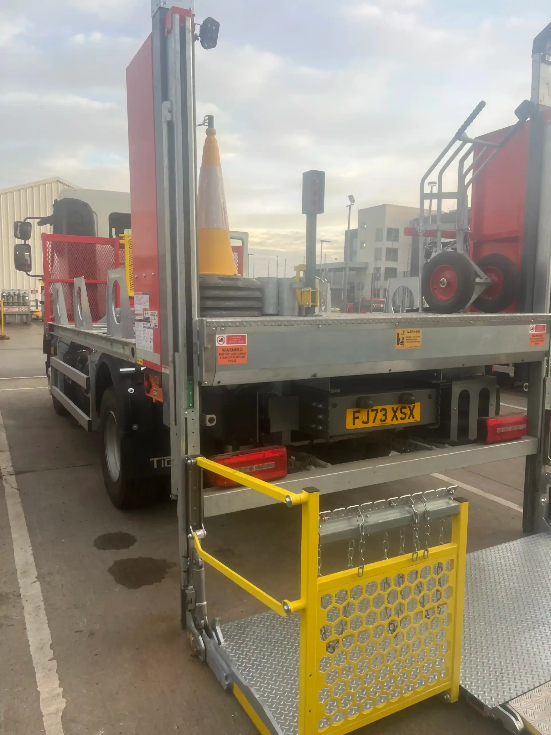 A rear view of a truck featuring a lowered, metal hydraulic tail lift platform with yellow safety railings.