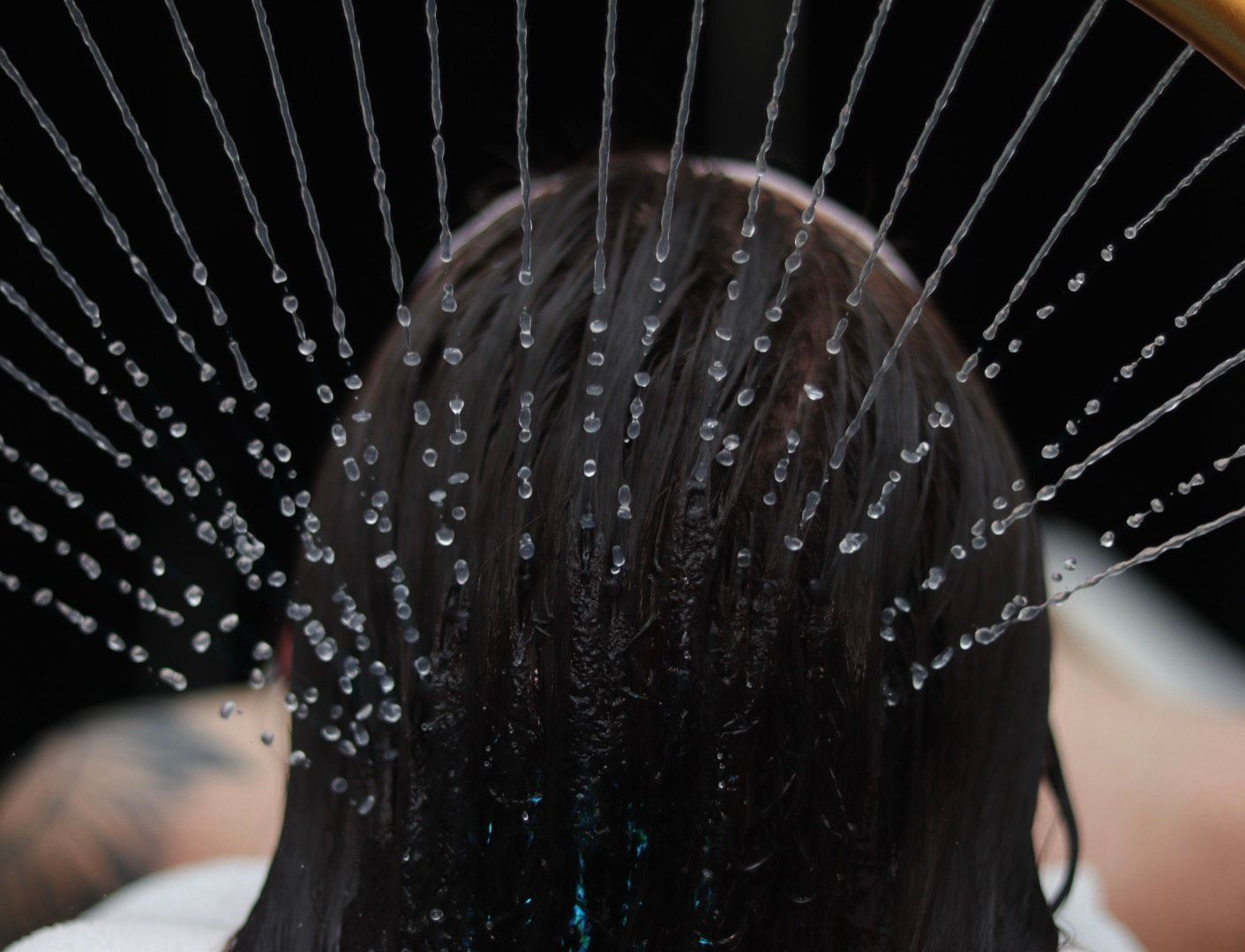 Person's head, wet hair, being sprayed with water. Dark background.