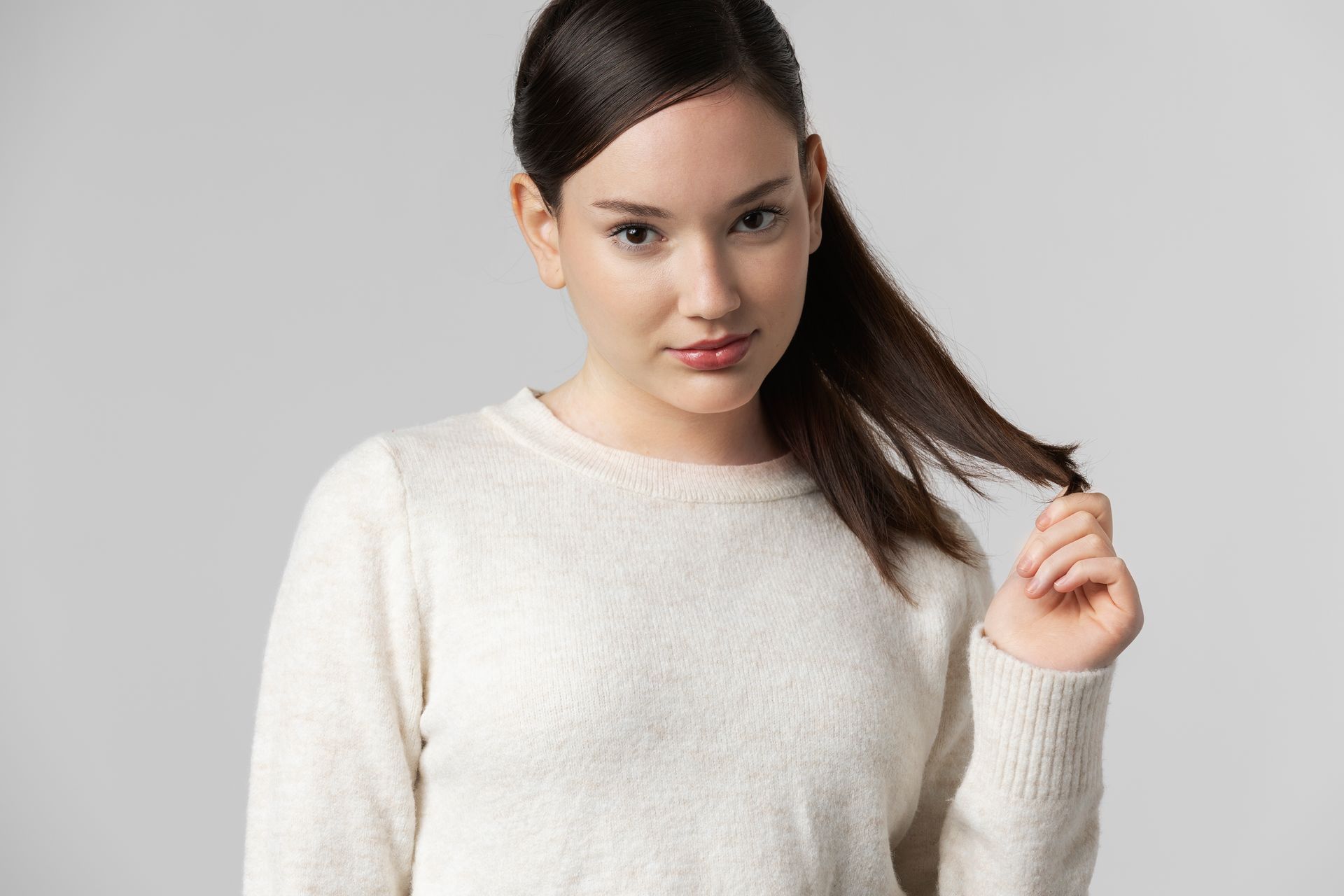 A woman in a white sweater is holding her hair in a ponytail.