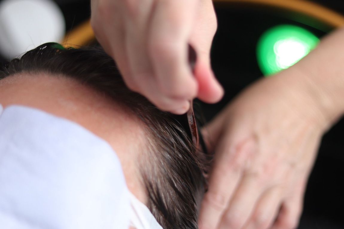 Hands styling wet hair near forehead; green light in background.