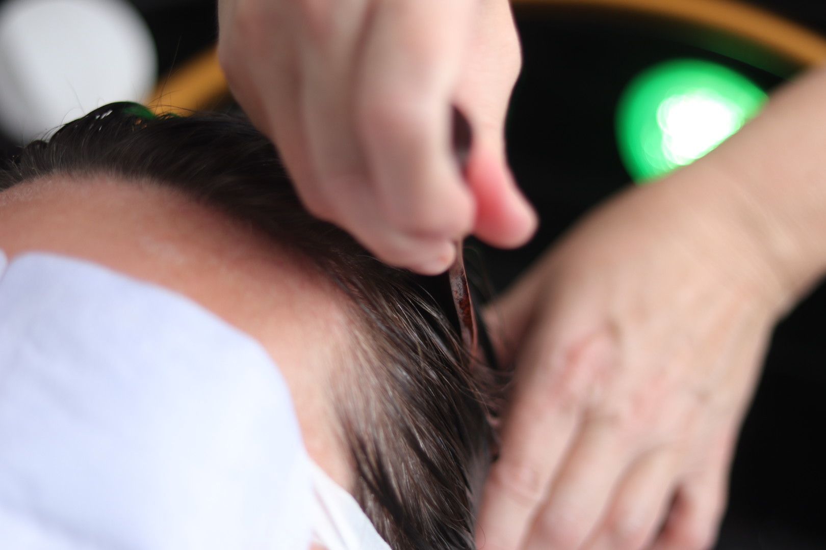 Hands styling wet hair near forehead; green light in background.