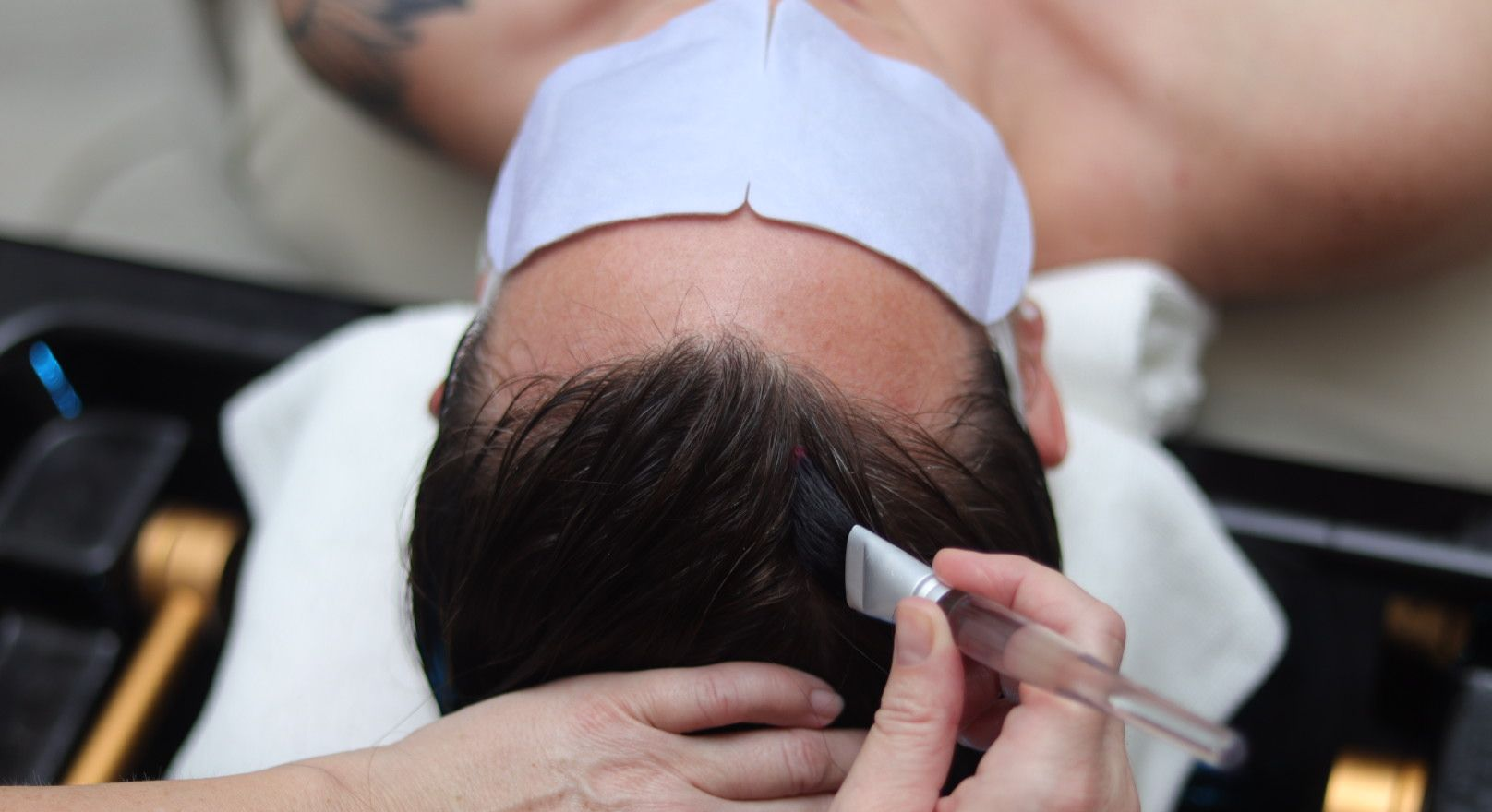 Water streams down a person's wet, dark hair. A golden, circular water source is above.