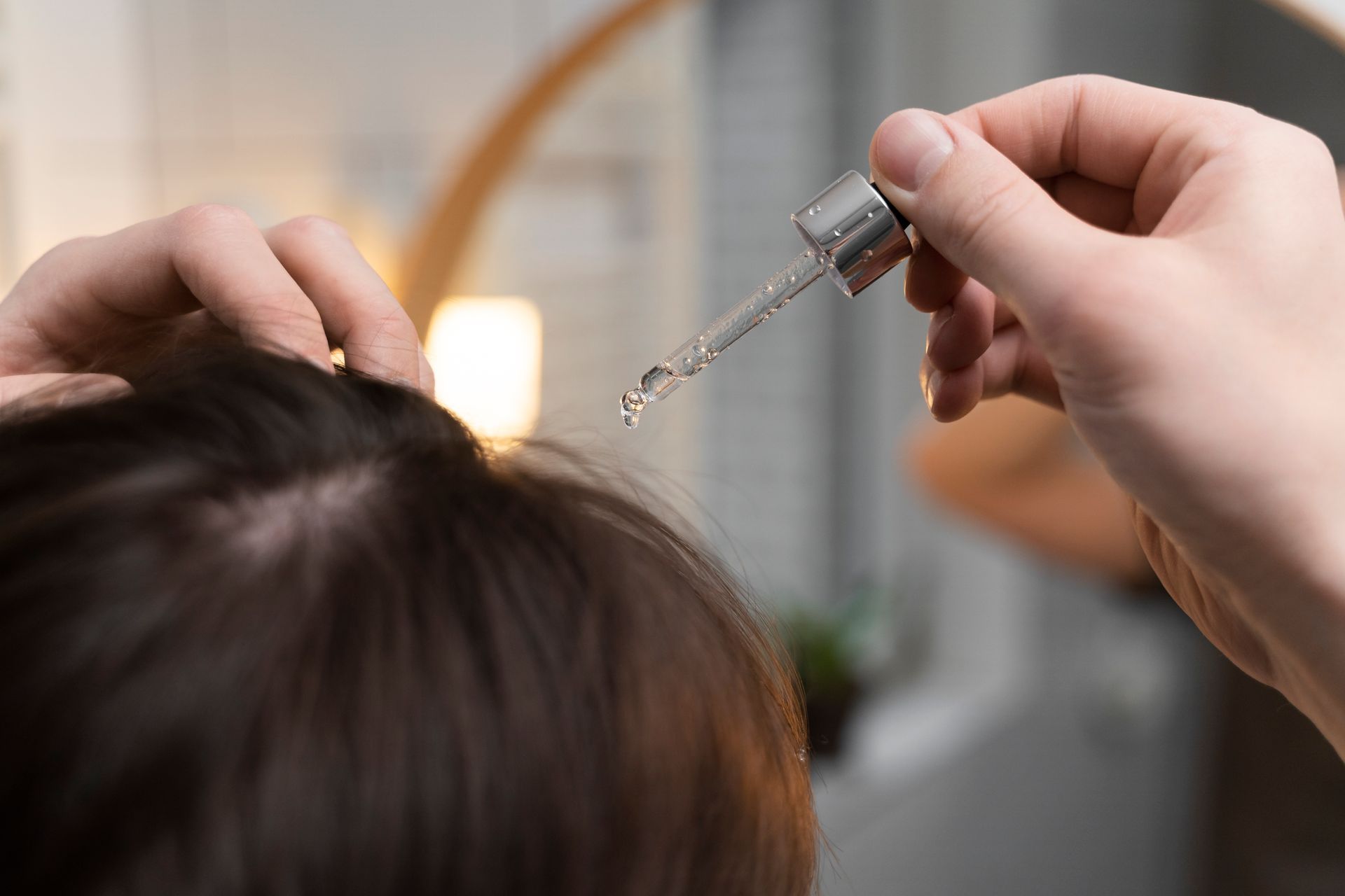 A woman is applying a serum to her hair with a pipette.