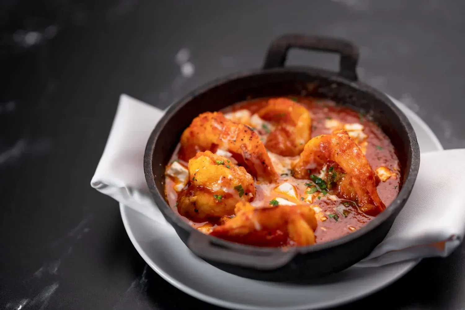 A bowl of shrimp in tomato sauce on a white plate