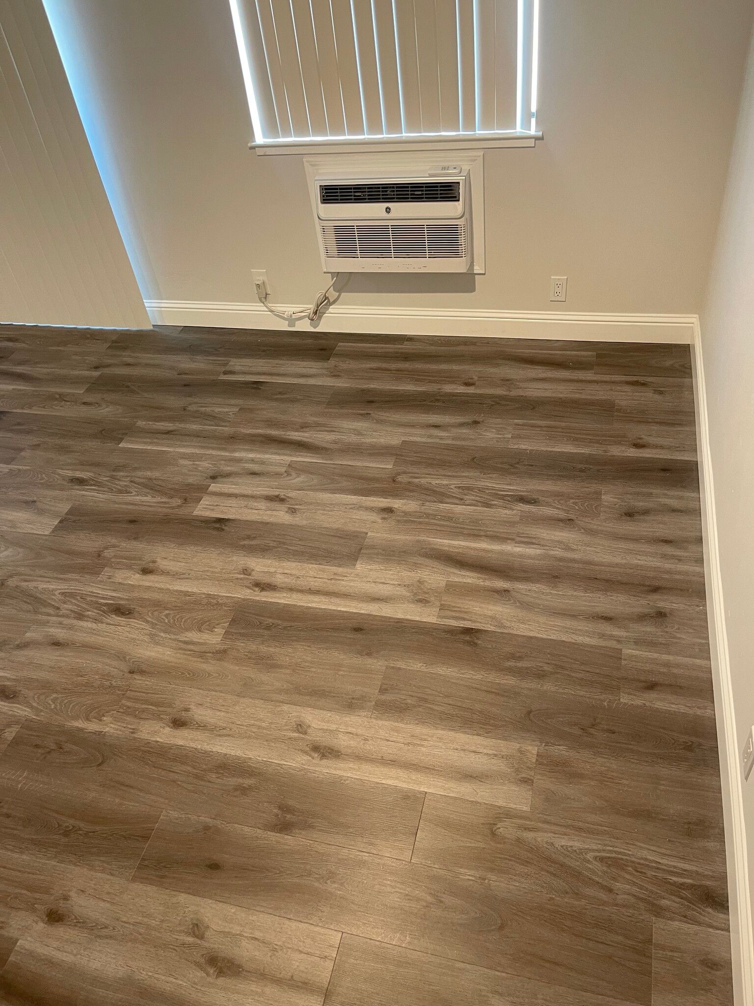 A room with hardwood floors and a window with blinds.