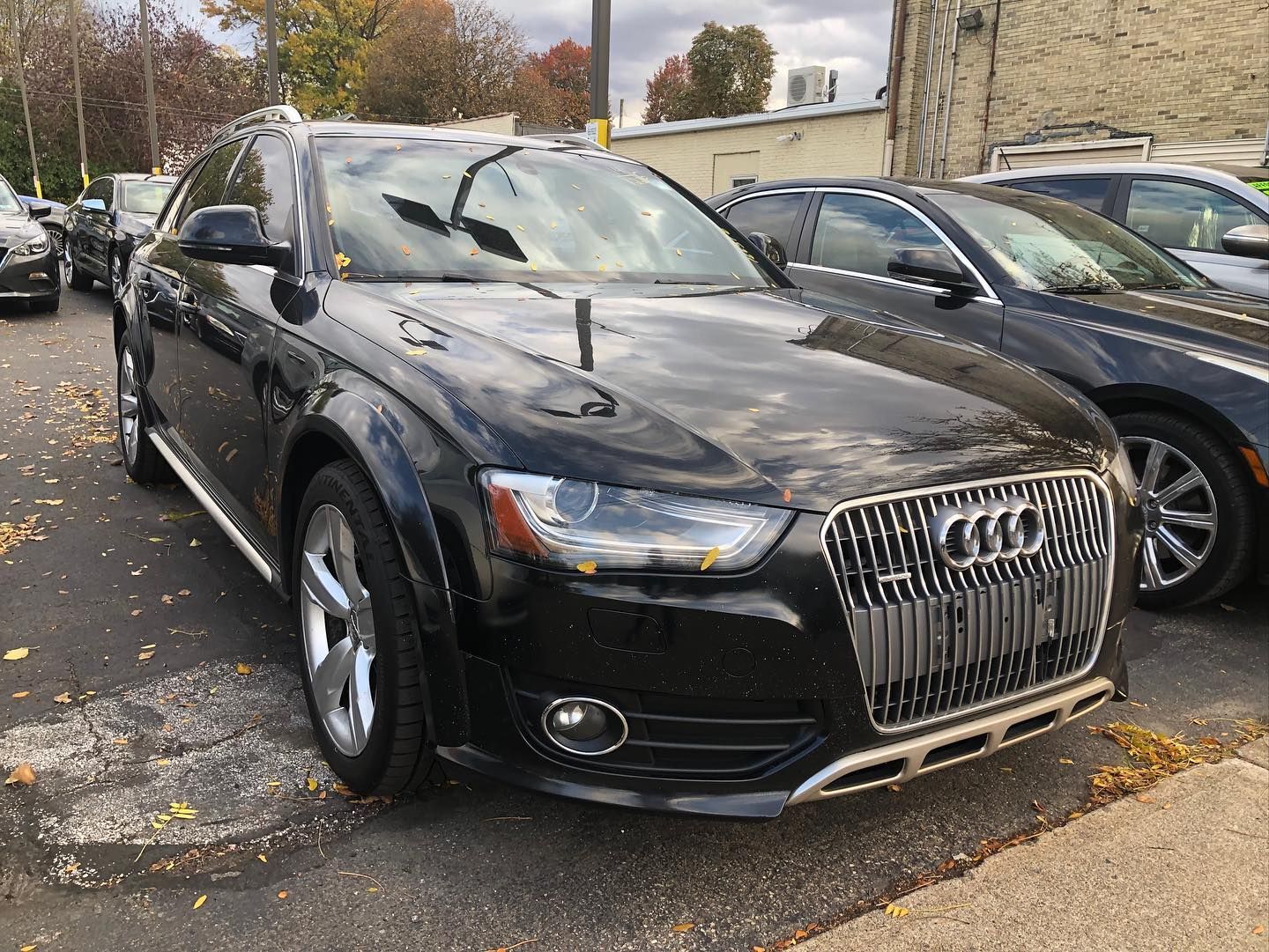 Black Audi Allroad wagon parked on pavement, facing the camera.